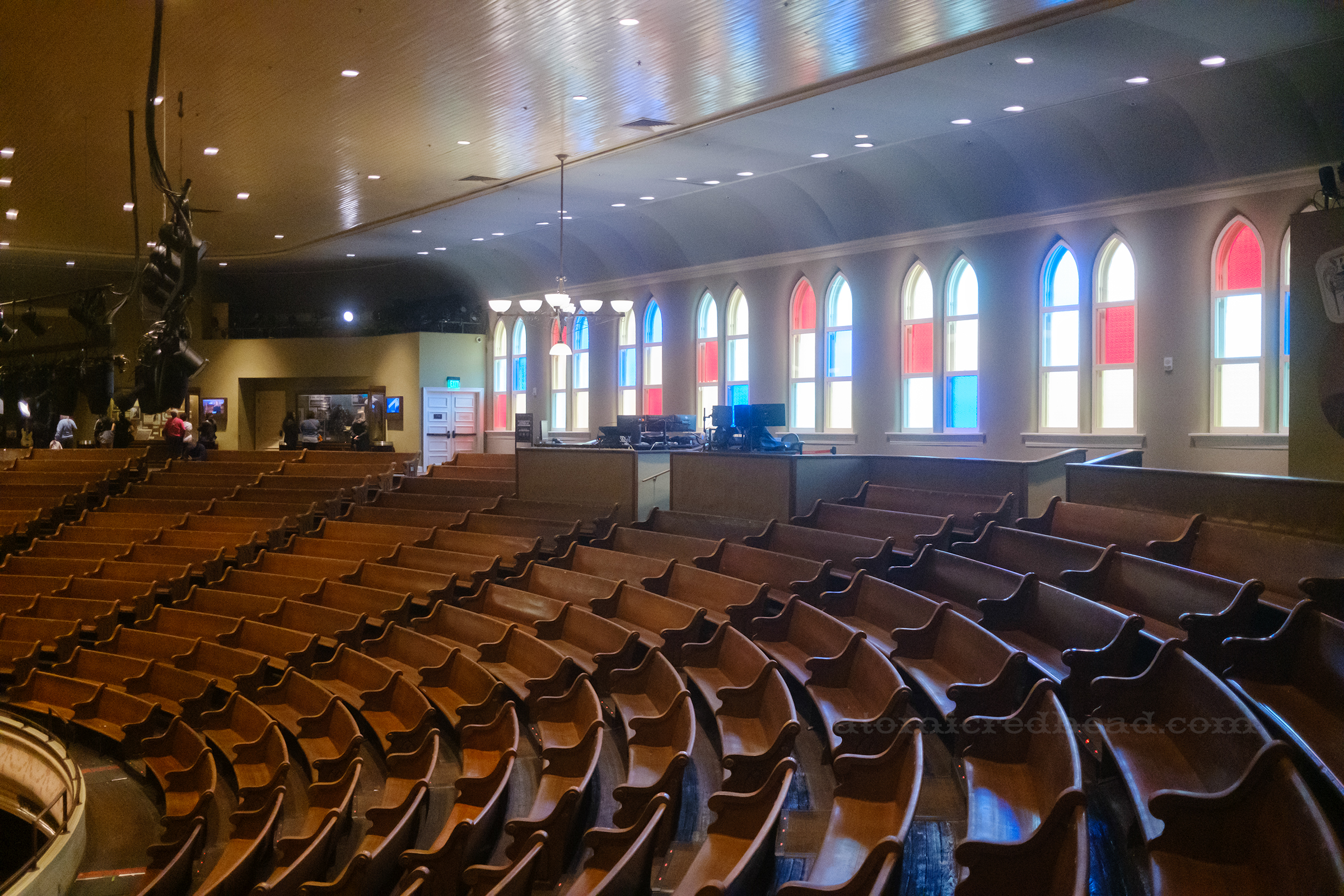View of the seating, with red, yellow, blue, and green stained glass behind.