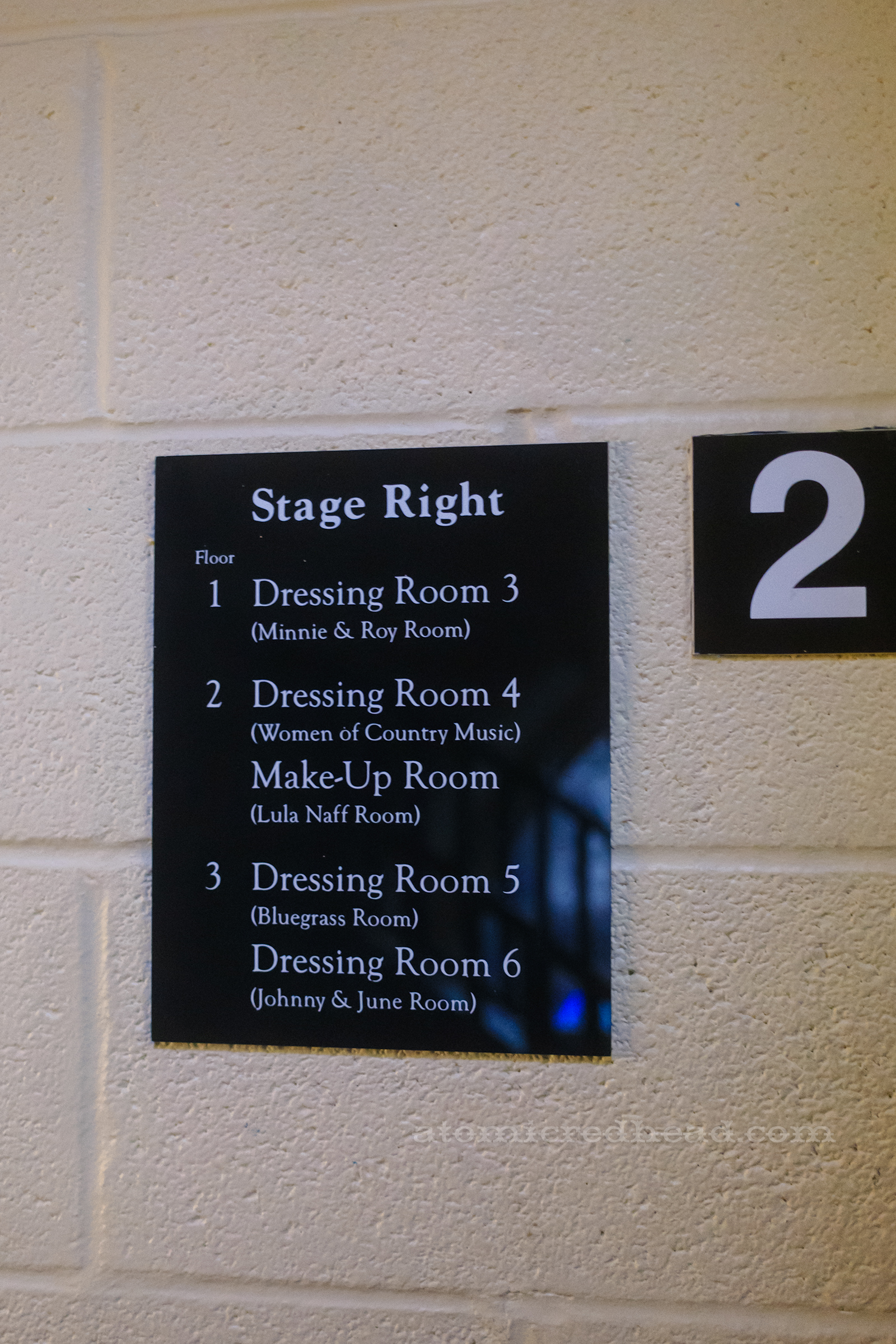 A black sign in the stairwell informs what is on each floor "Stage Right Floor 1 Dressing Room 3 (Minnie & Roy Room) 2 Dressing Room 4 (Women of Country Music) Make-Up Room (Lula Naff Room) 3 Dressing Room 5 (Bluegrass Room) Dressing Room 6 (Johnny & June Room)