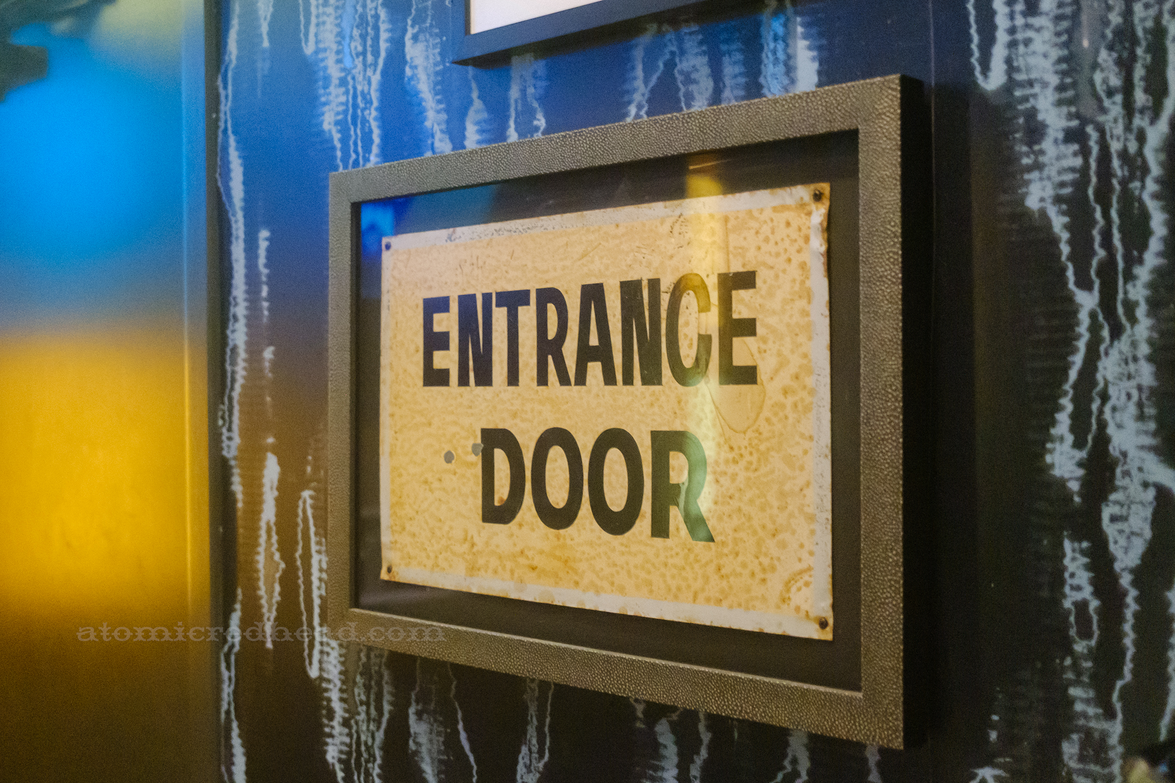 A vintage sign, framed, reading "Entrance Door" in black letters.