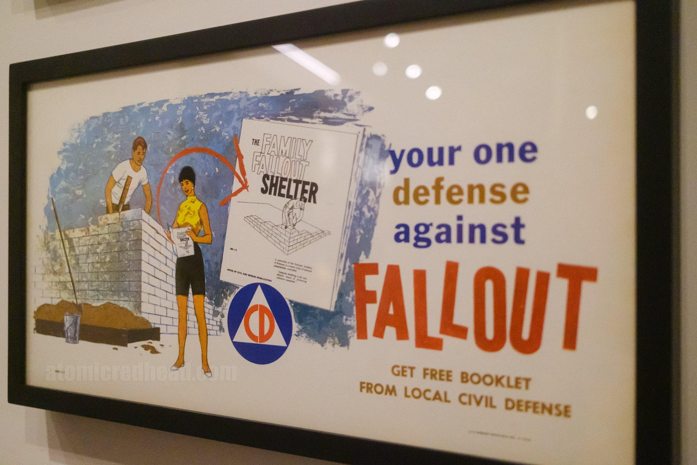 A small poster with a couple building a bomb shelter and a booklet with "Family Fallout Shelter" on the cover, to the right text reads "Your one defense against fallout get free defense from local Civil Defence"