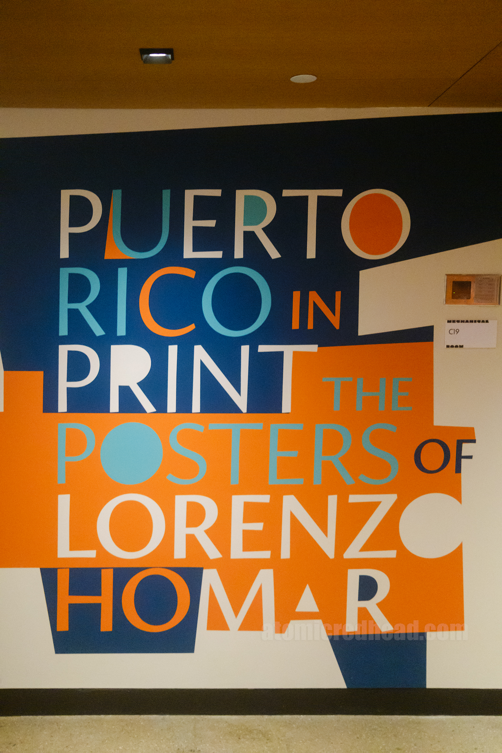 A large blue and orange wall graphic reading "Puerto Rico in Print the Posters of Lorenzo Homar"
