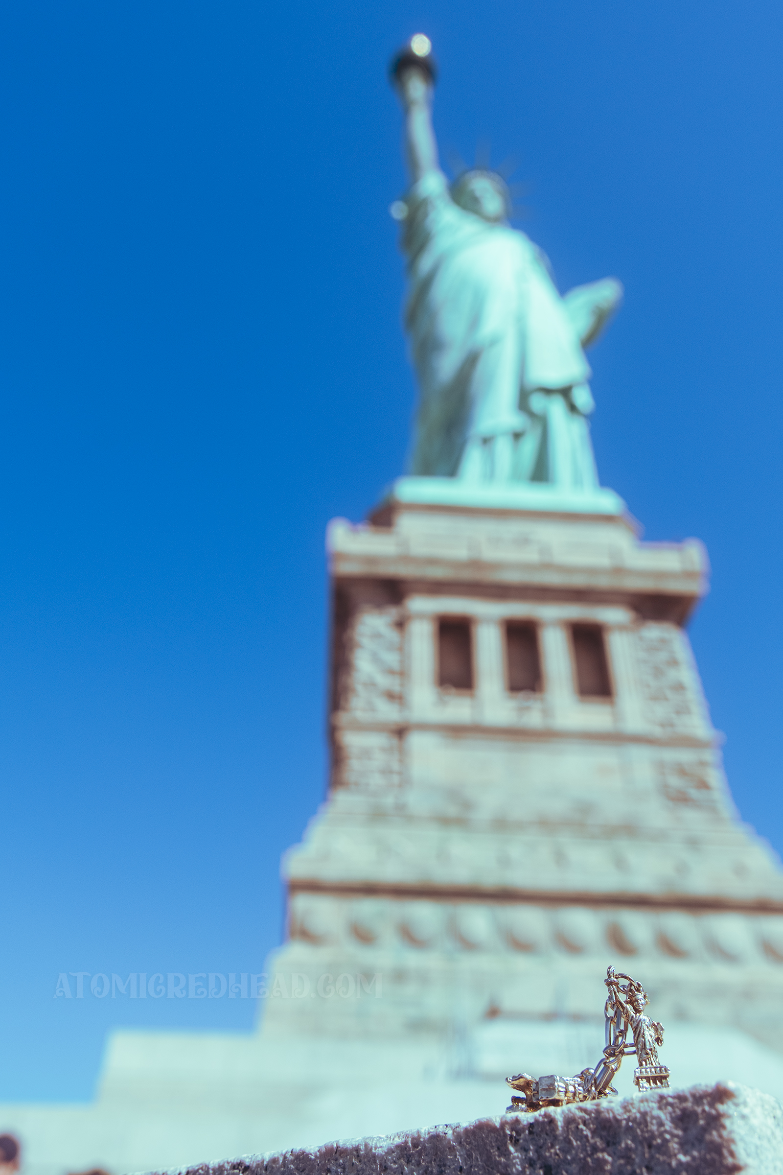 In the foreground, a tiny Statue of Liberty from my charm bracelet, standing in front of the real thing.