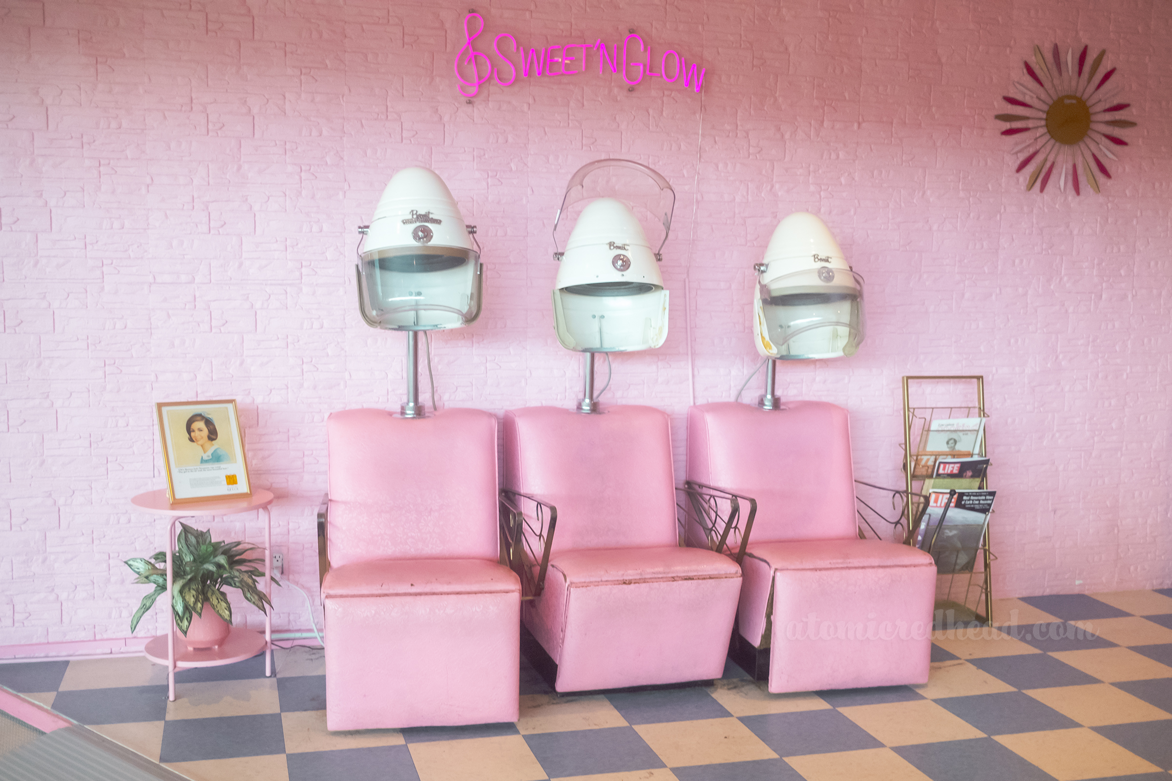 The faux beauty parlor, with a pink stone wall, with pink hair dryer salon chairs in front.