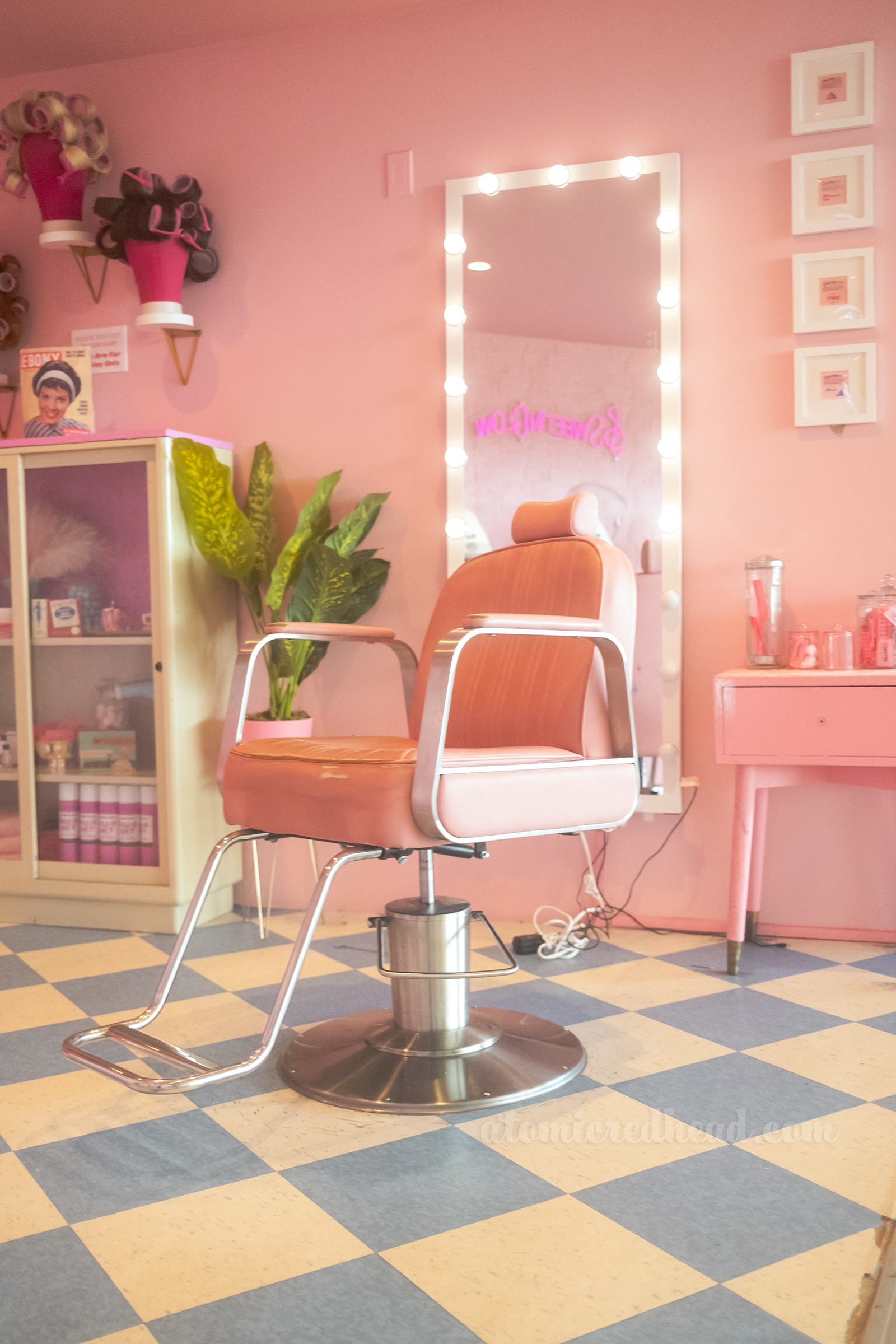 A pink salon chair sits in front of a pink wall with a long mirror behind.