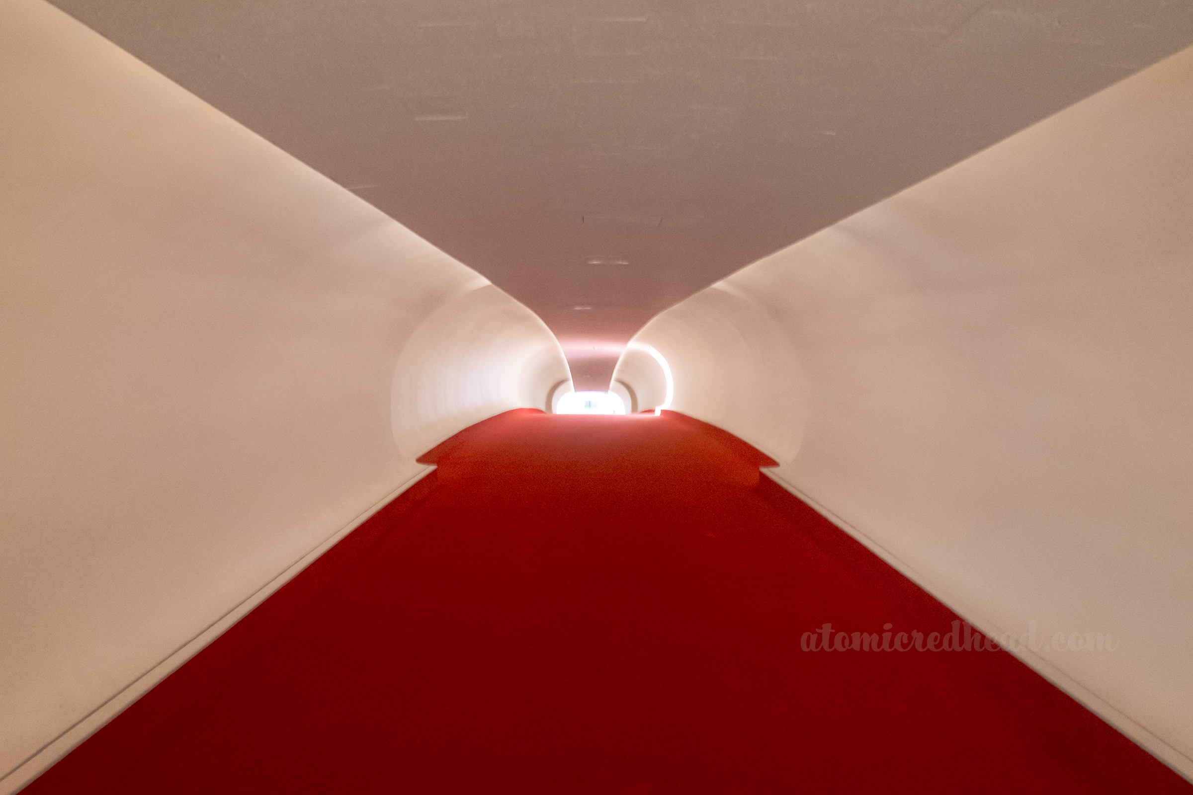 Looking down the white tube hallway with red carpet.