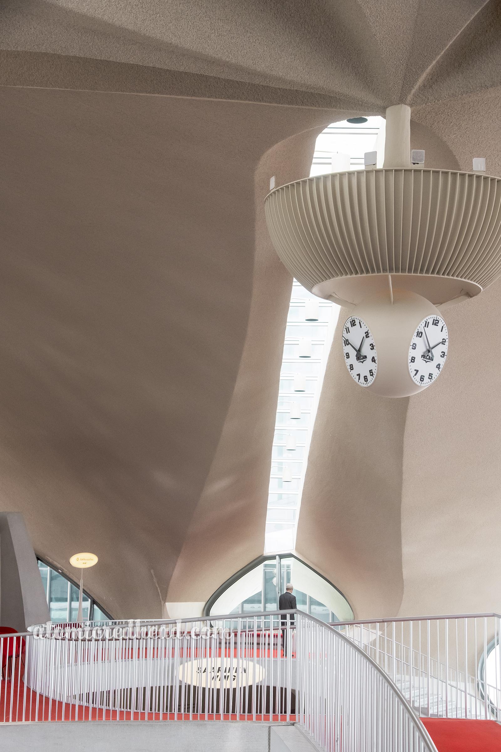 A clock hangs from the middle of the lobby with a bridge under it.