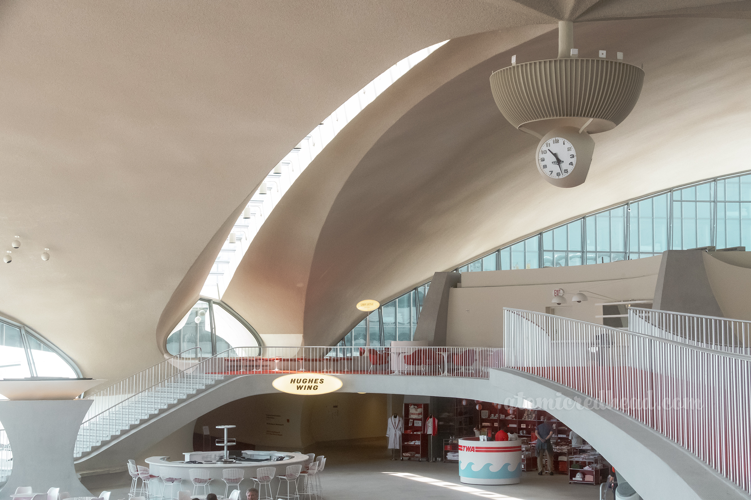 Overall of a portion of the lobby, with a clock hanging above a bridge that connects the upper floor.