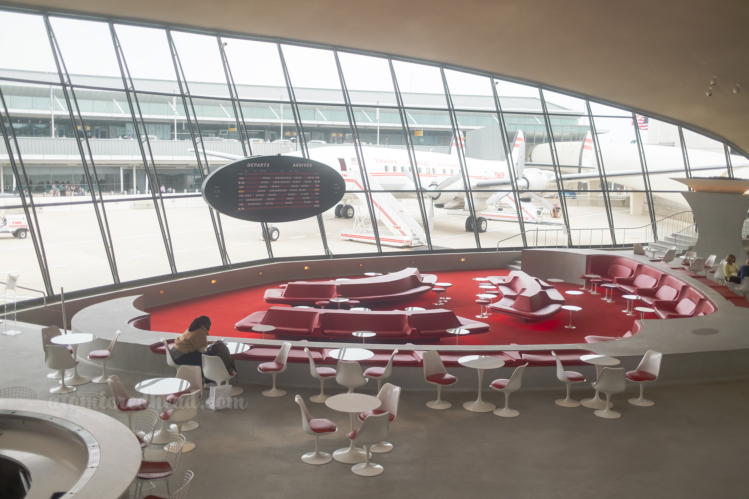 The sunken lounge rests in front of a massive window overlooking a vintage airplane.