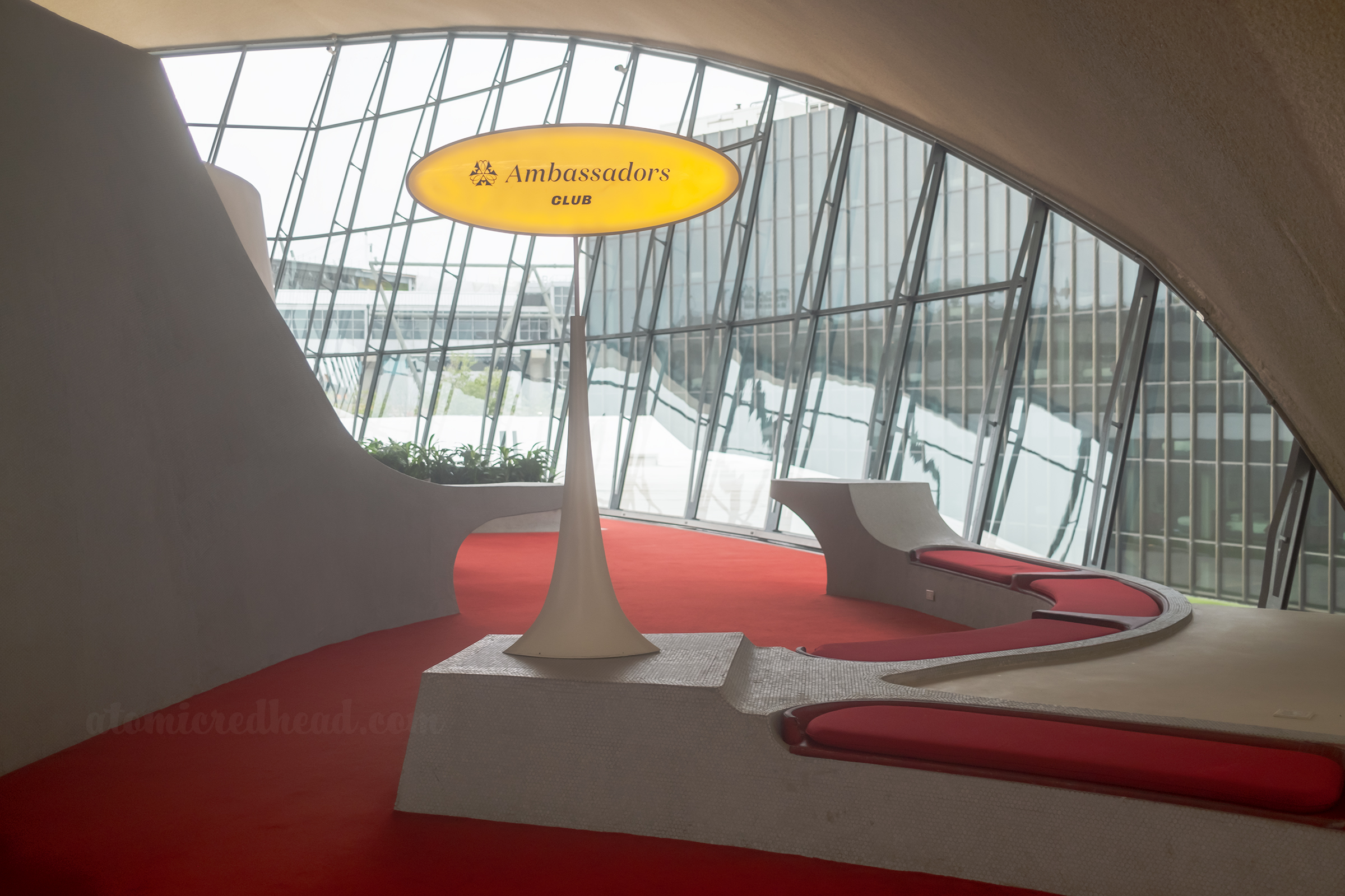 An oval lighted sign reads "Ambassadors Club" and leads to built in seating with red carpet and red upholstery. 