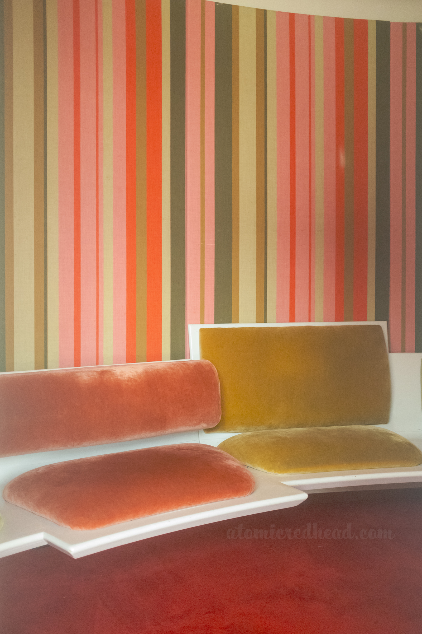 Pink, gold, green, and cream stripe wallpaper meets a pair of built in seats upholstered in orange and olive velvet.