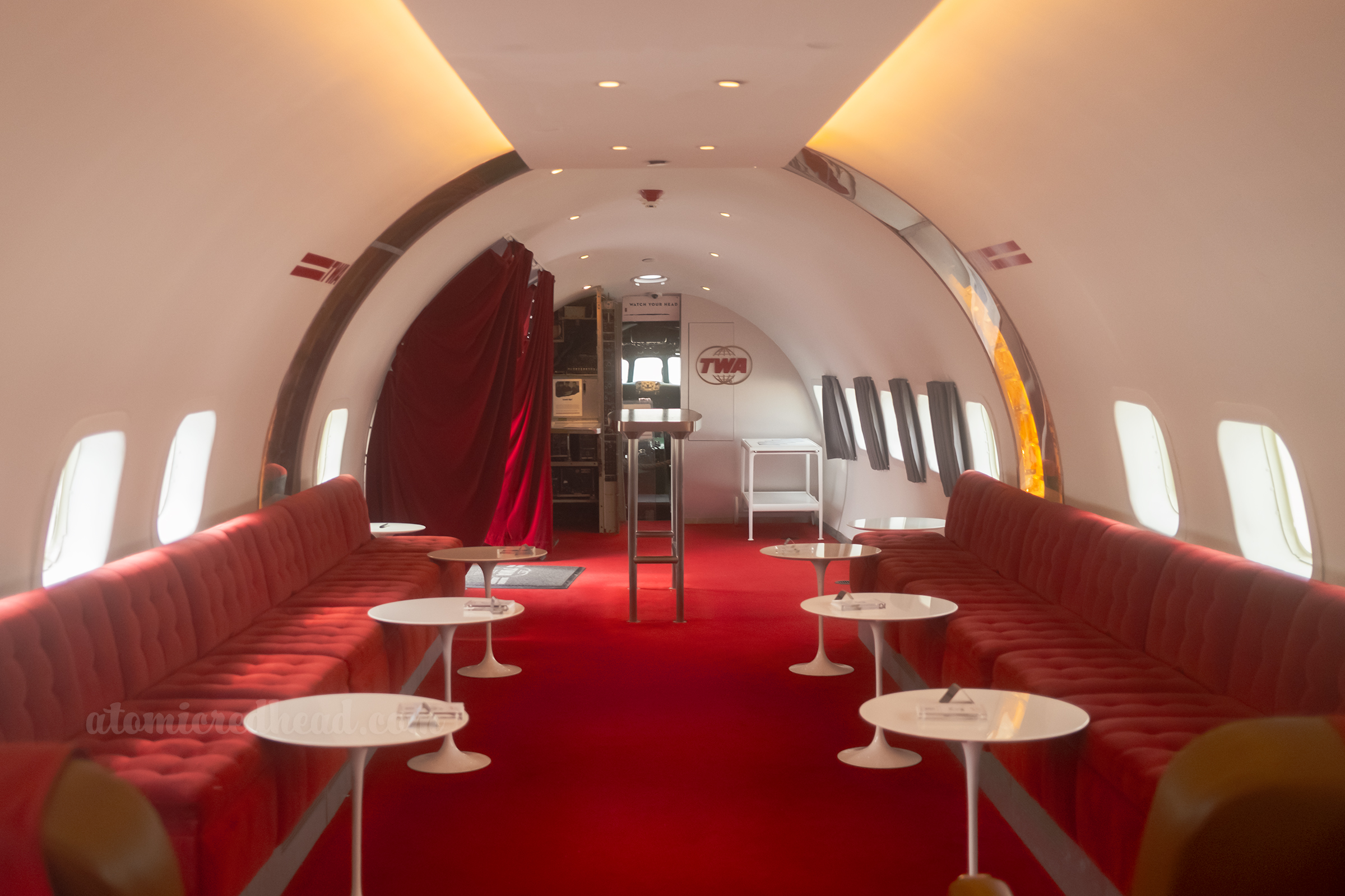 Interior of the Connie bar, with build in bench seating upholstered in red, and small circular white tables.