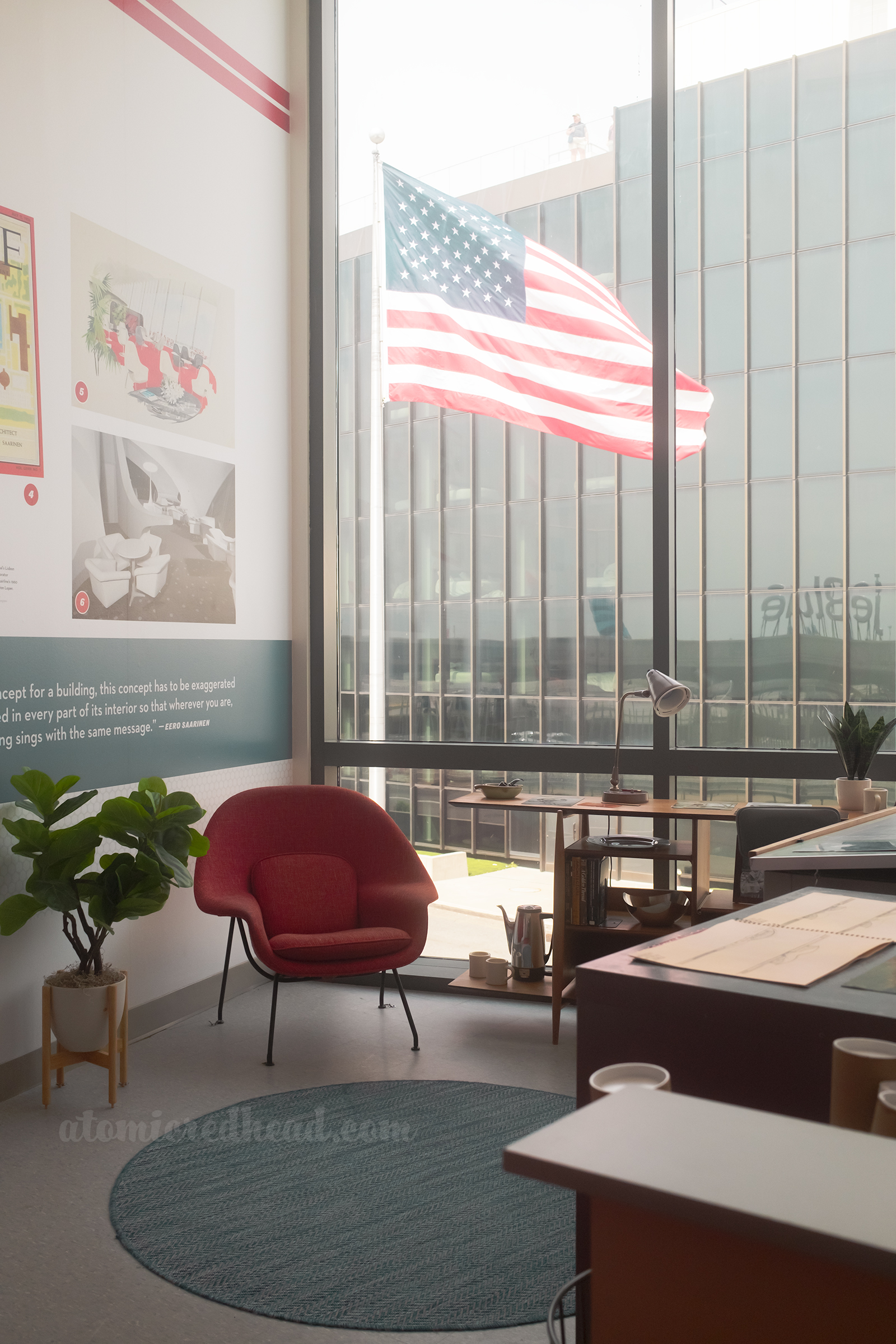 A mock up of Saarinen's office, with a red "Womb" chair on the left and a desk with papers on the right.
