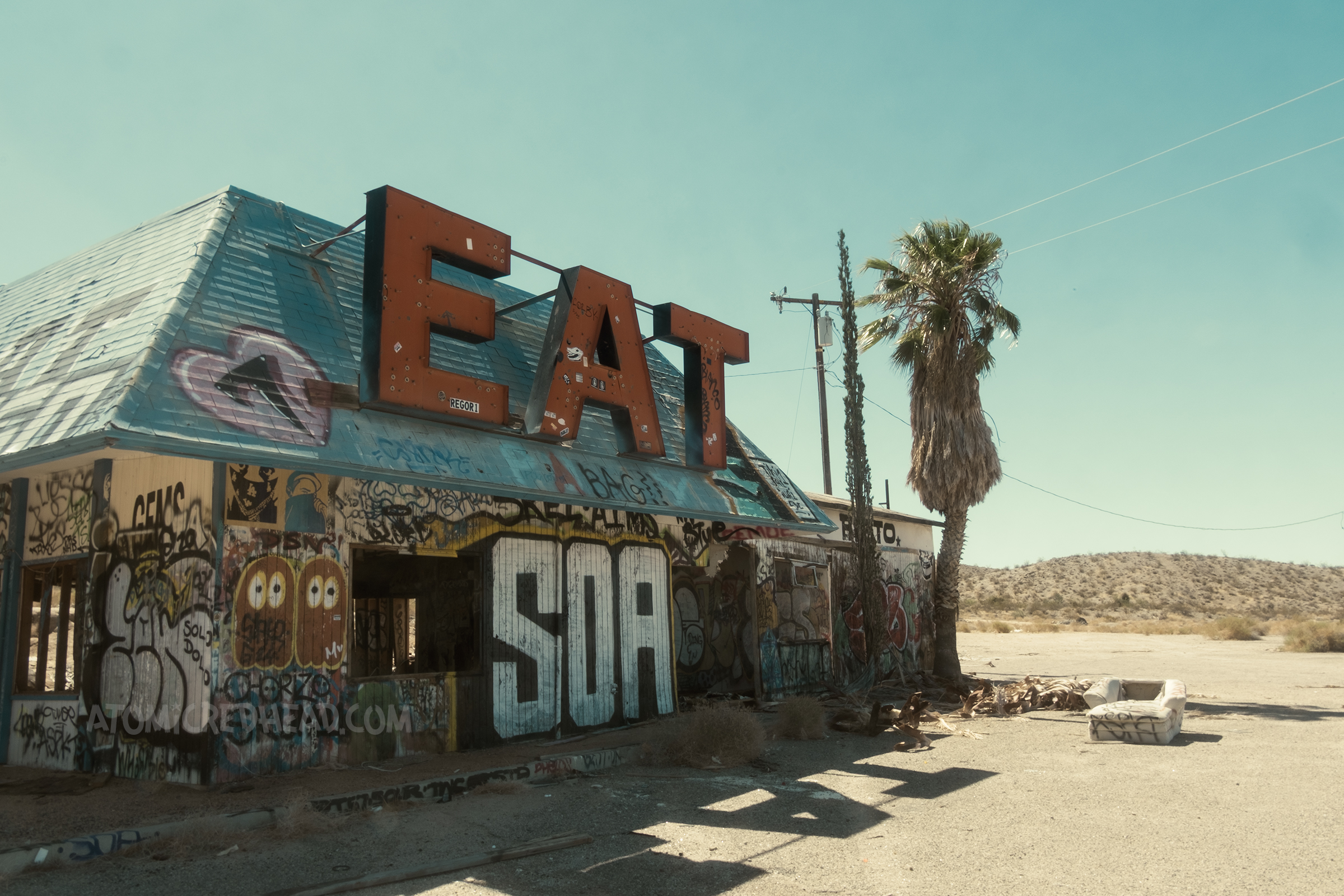 Exterior of the restaurant. Hanging from the blue roof are large red letters that read "EAT" and the remainder of the building is covered in graffiti.