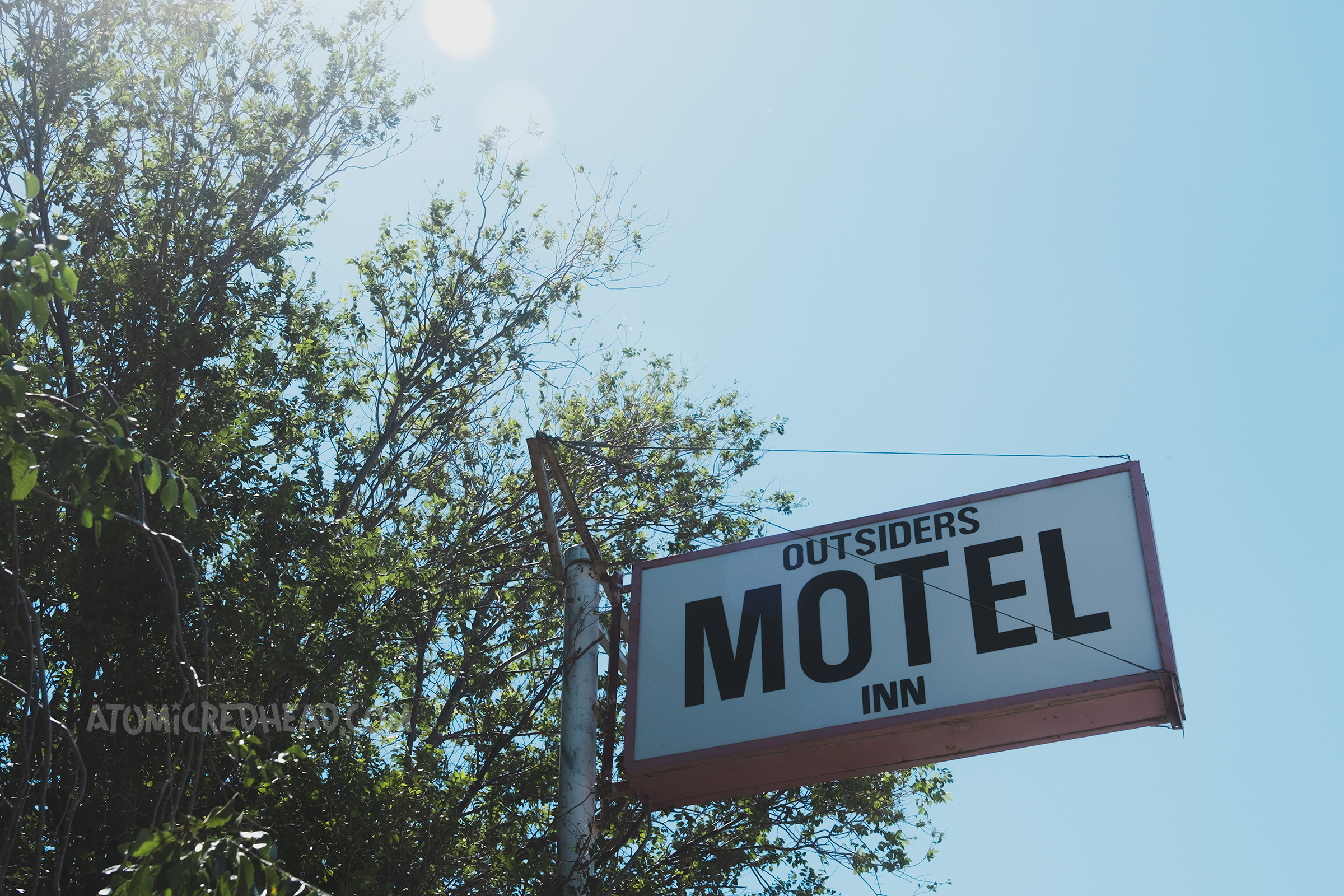 A black and white backlit plastic sign appears from an overgrown tree with text reading "Outsiders Motel Inn"