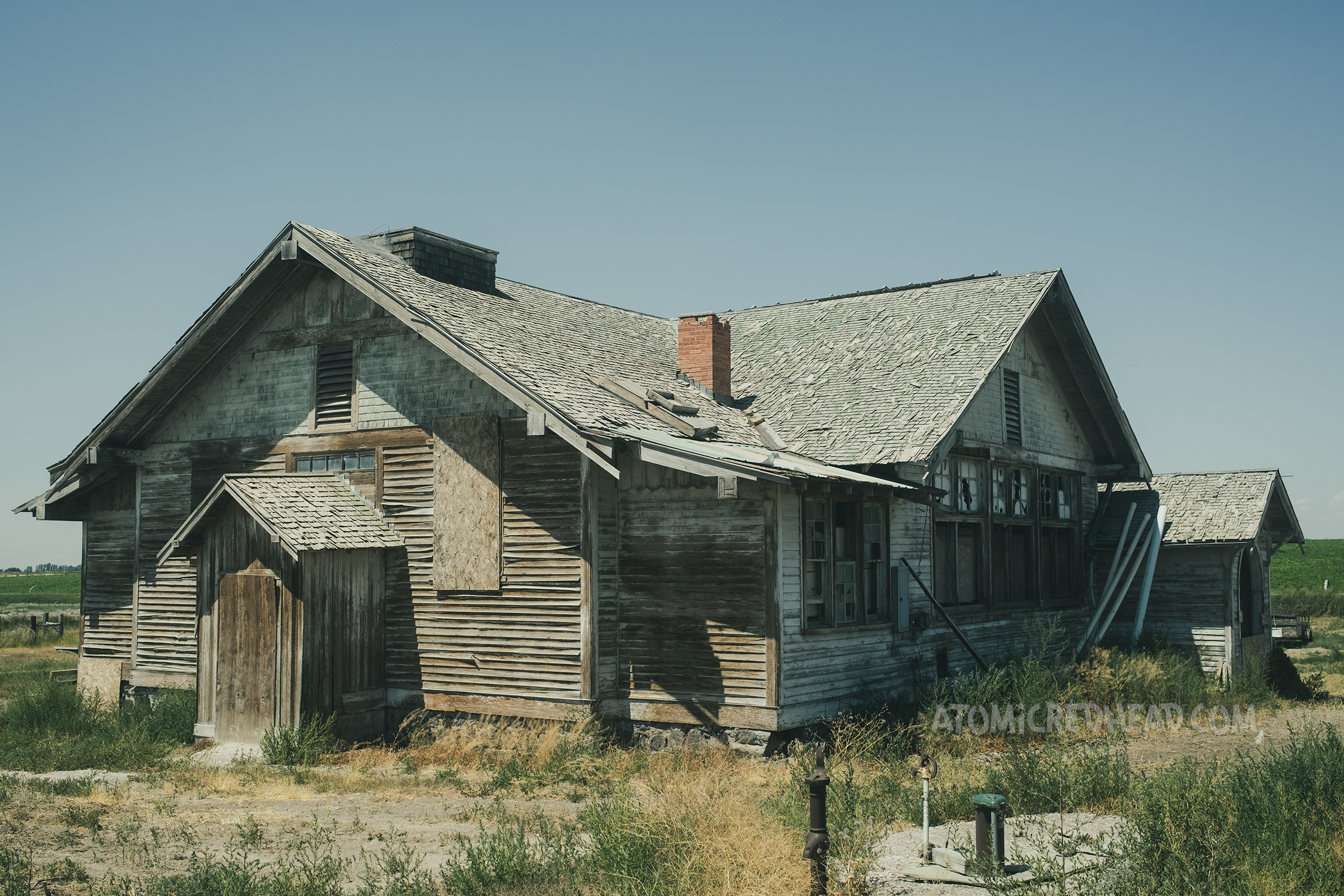 A large abandoned building with flaking white paint and boarded up windows.