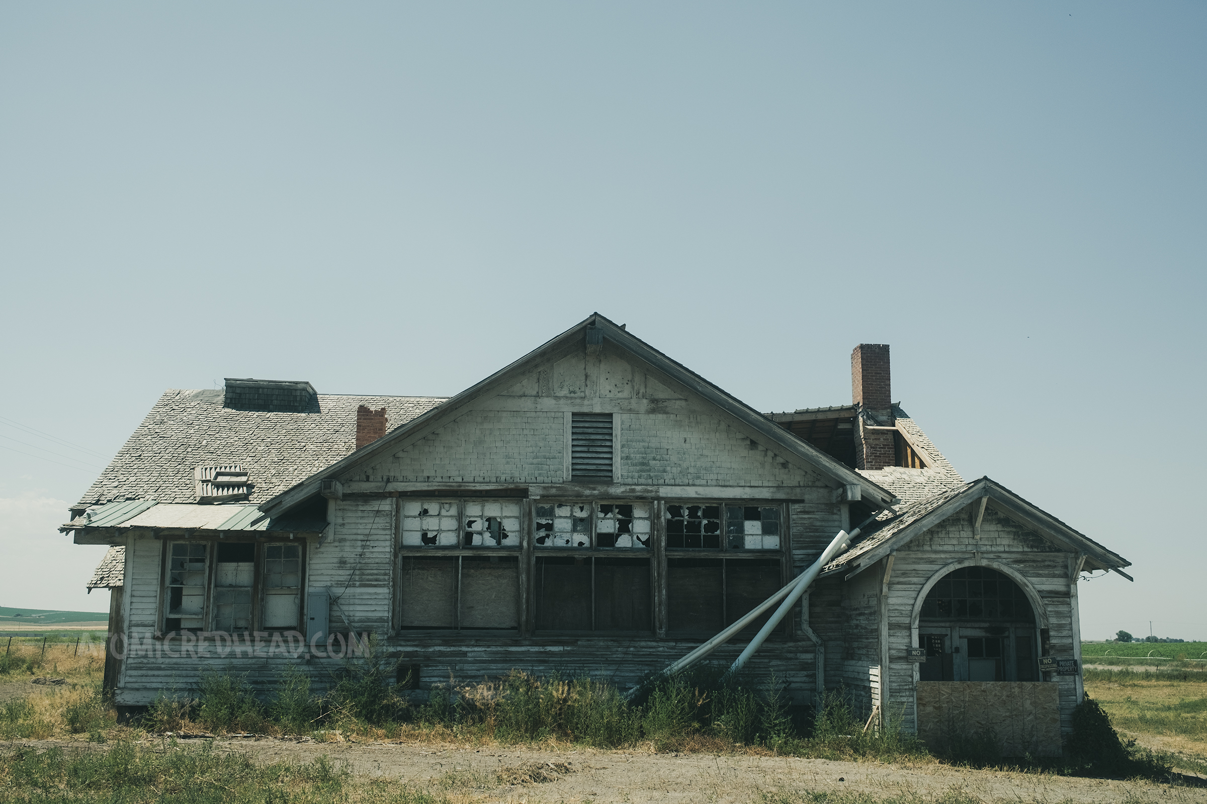 A large abandoned building with flaking white paint and boarded up windows.