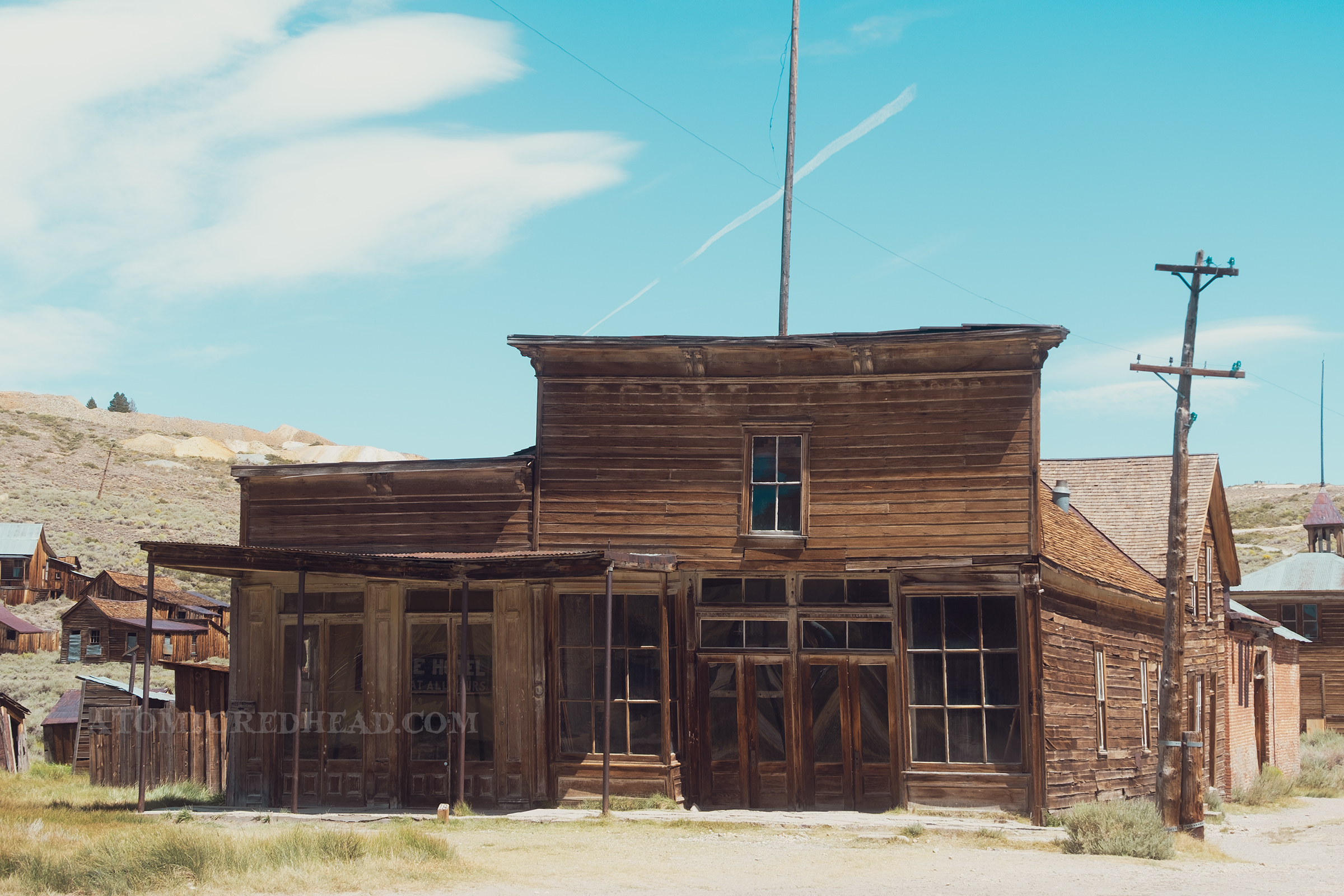 Two single story wooden structures with dark windows, former hotel and store.