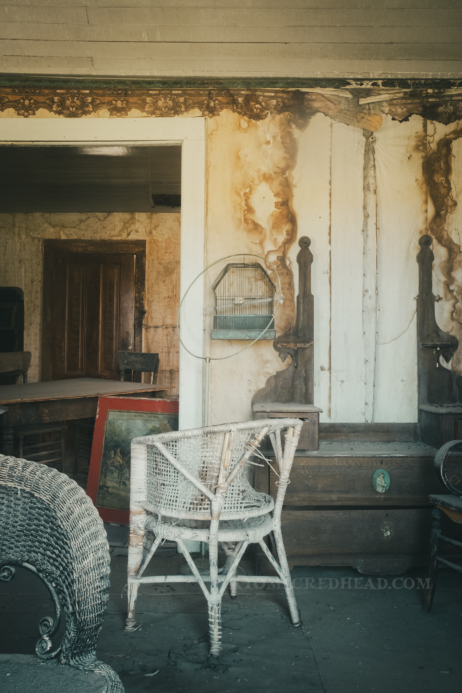Victorian furniture sits in an old house with water damaged wallpaper.