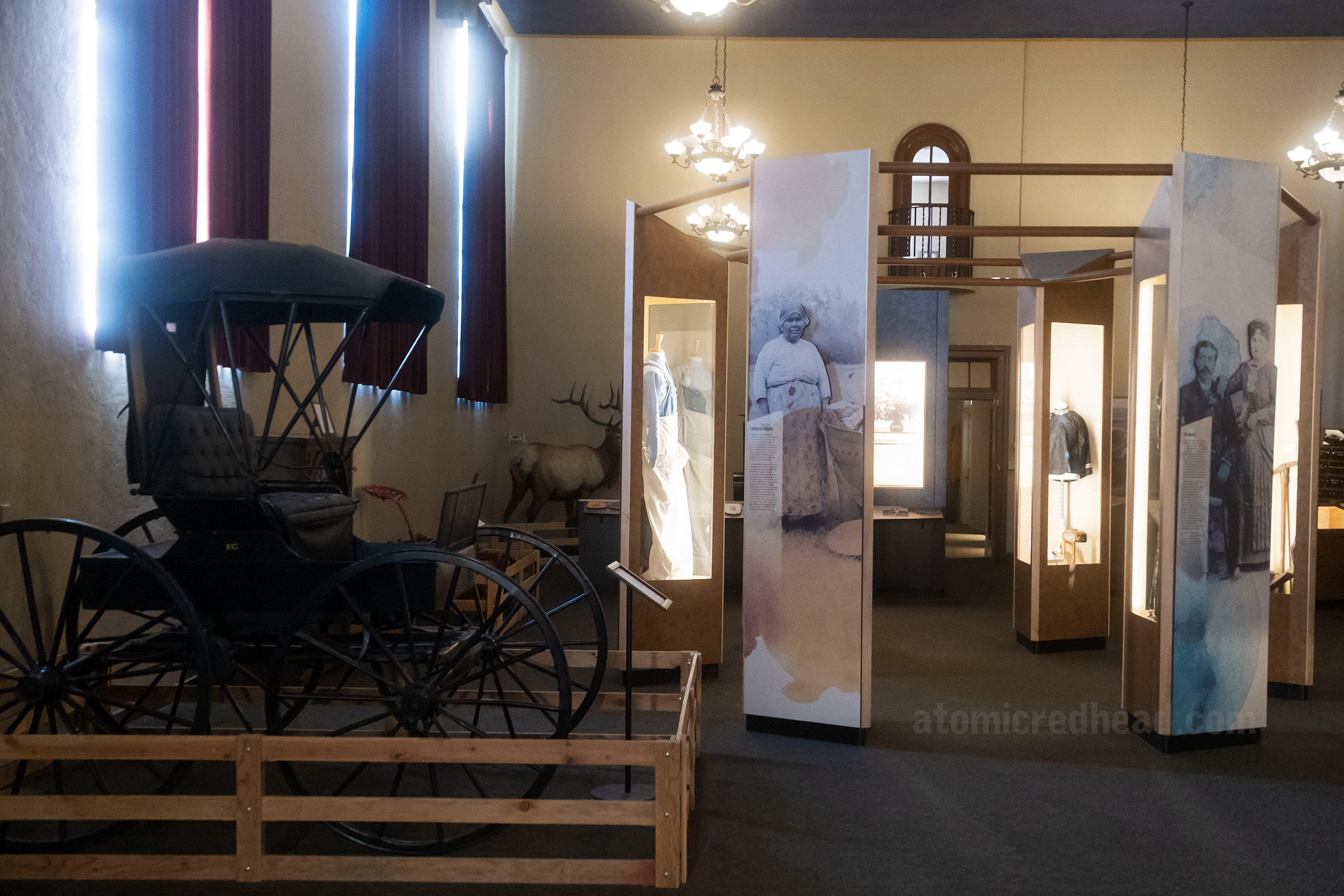 Overall view of an interior gallery with a carriage and antique clothing.