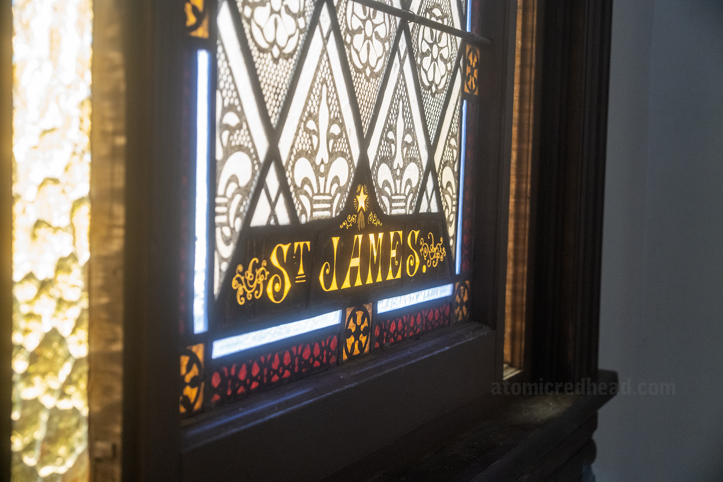 Closeup of stained glass with "St. James" in yellow at the bottom.