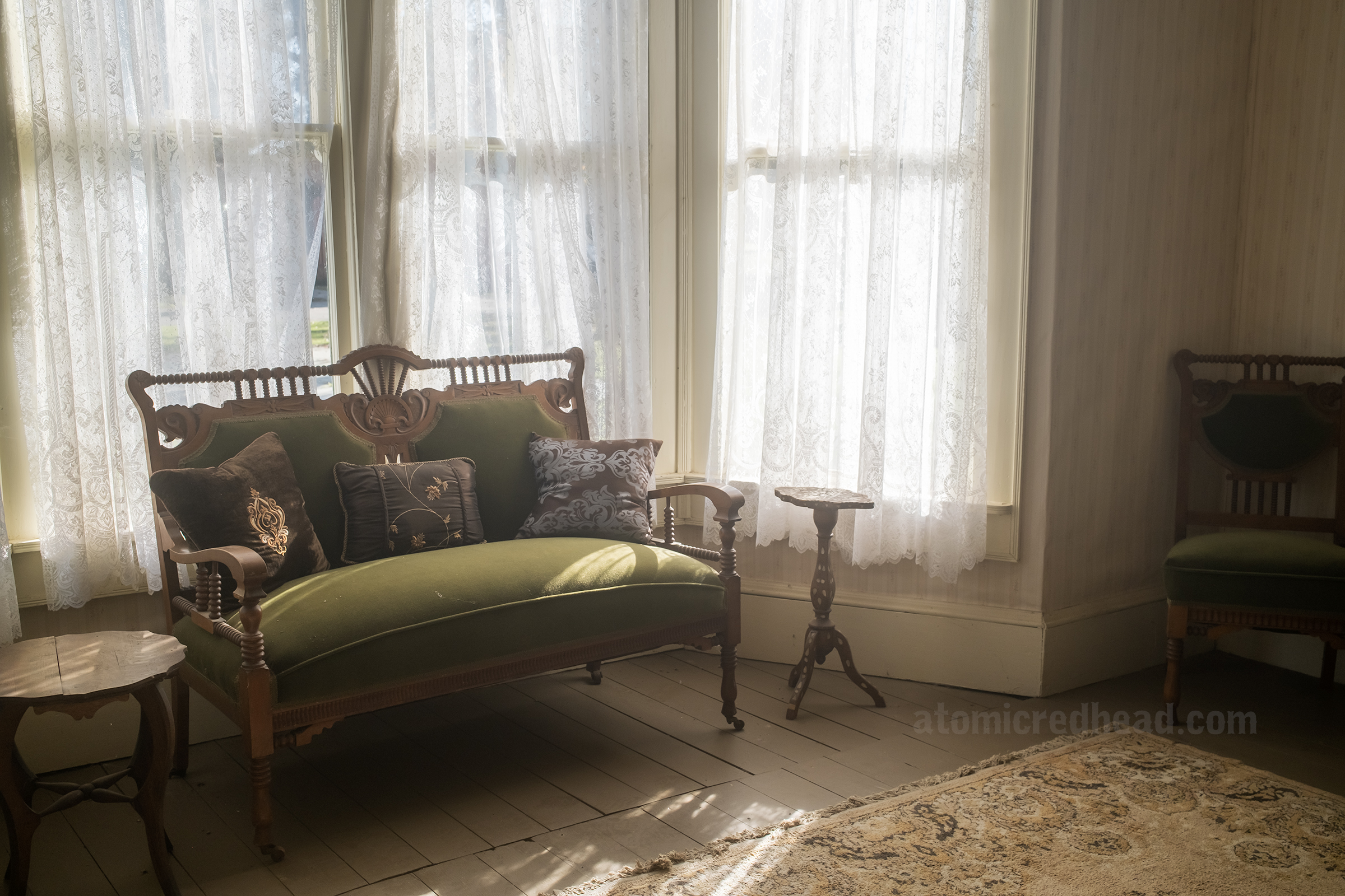 An olive colored love seat sits in a bay window.