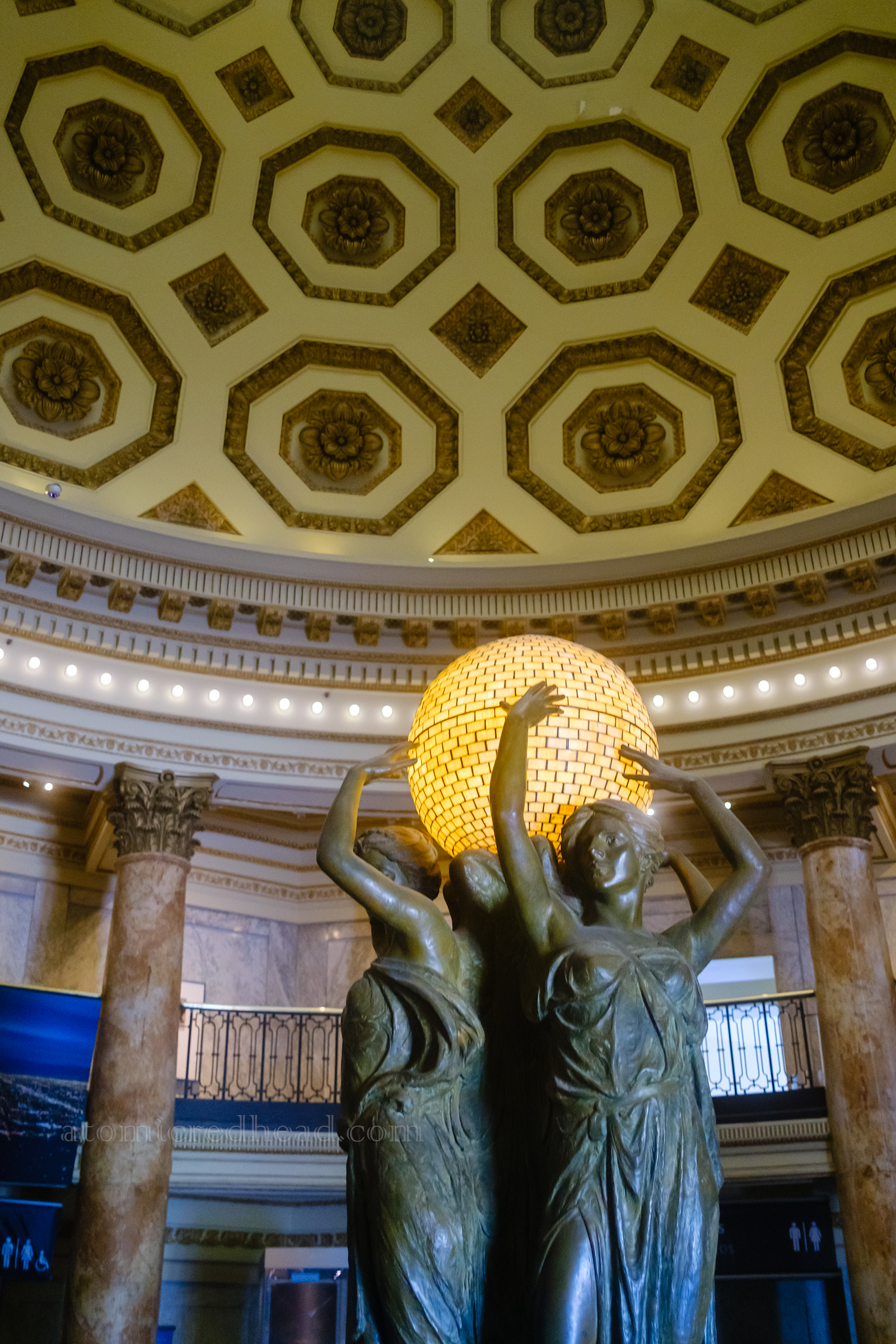 Three statues of women hold up a round glass light.