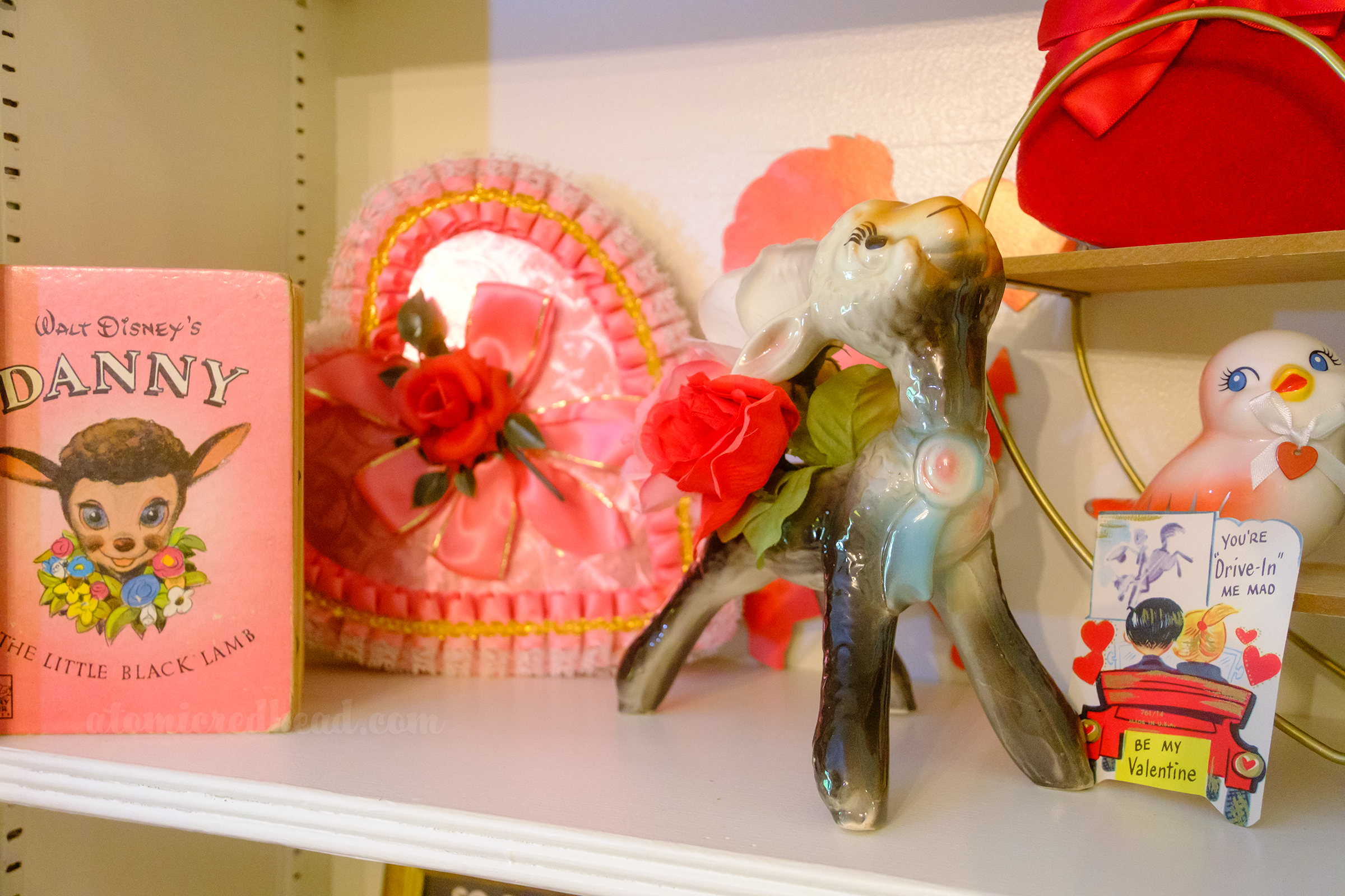 Close-up of a ceramic planter shaped like Danny the lamb, sitting in front of a heart shaped chocolate box and a pink book of Danny the Lamb.