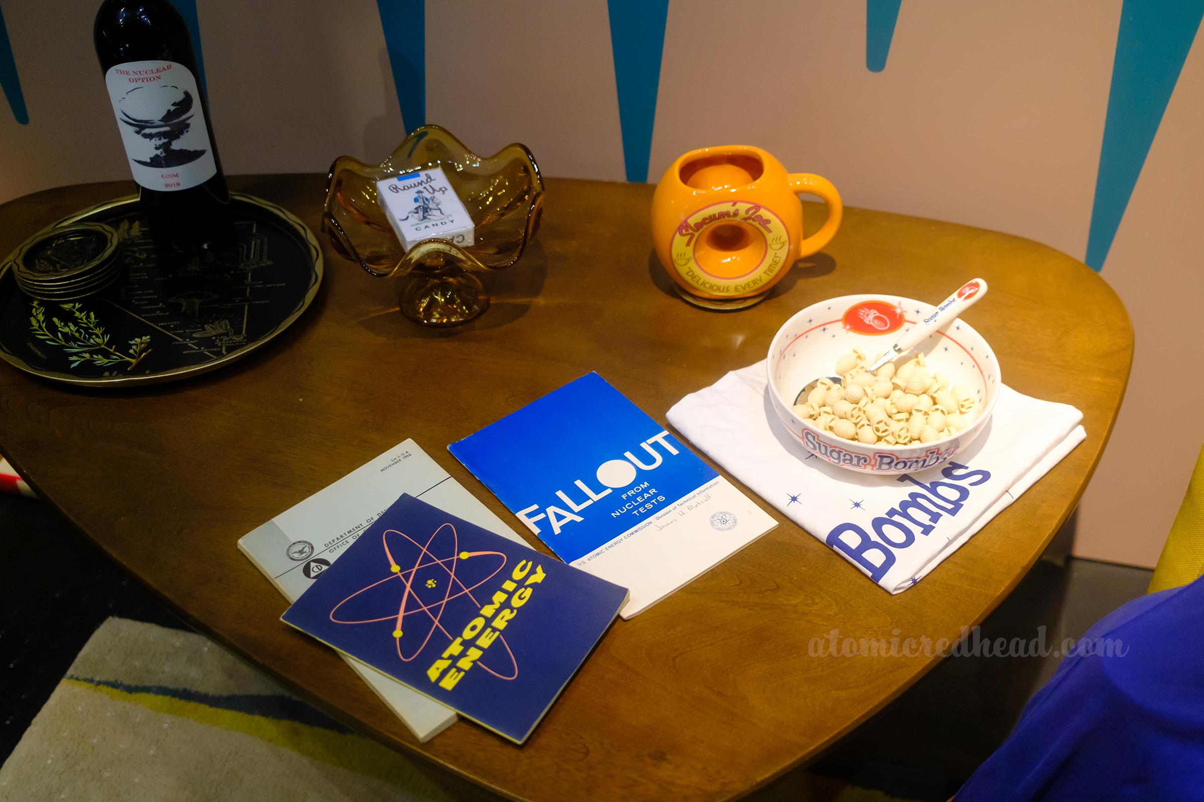 A vintage coffee table features brochures about atoms, fallout, and a bowl filled with Sugar Bombs.