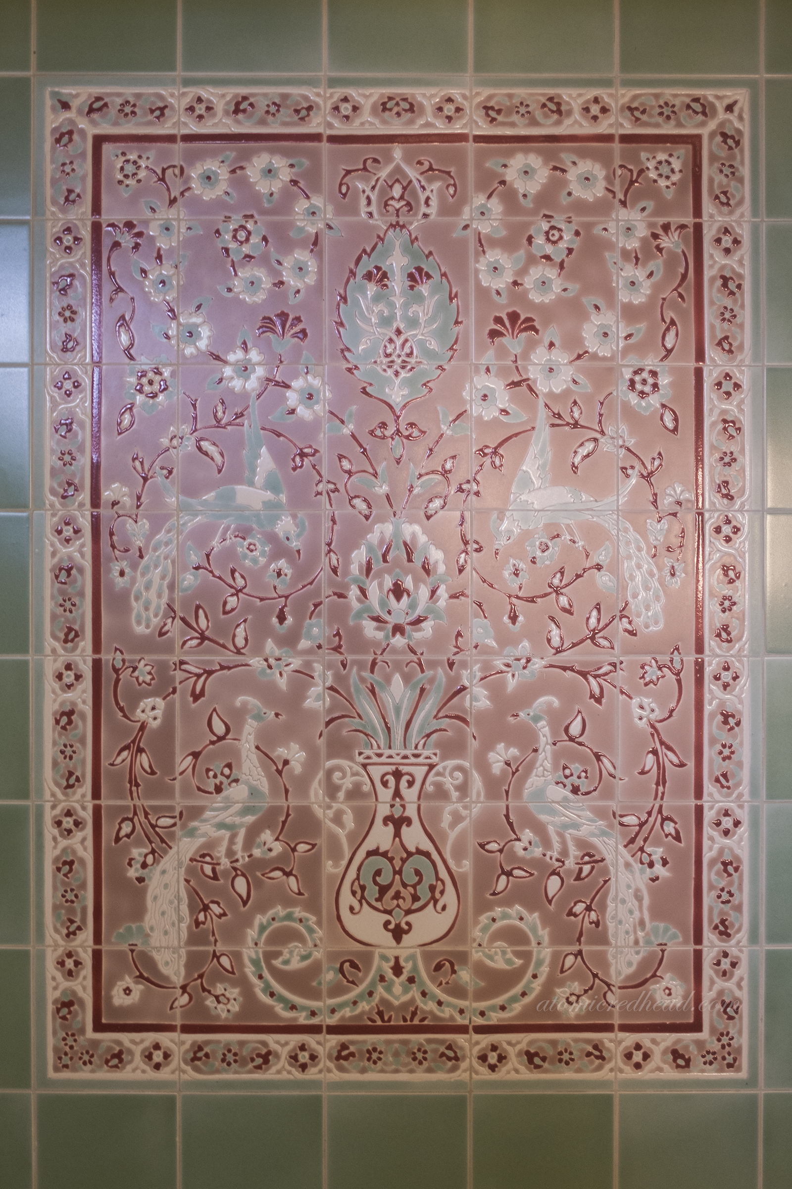 Close-up of a tile mural above a bath with flowers and peacocks.