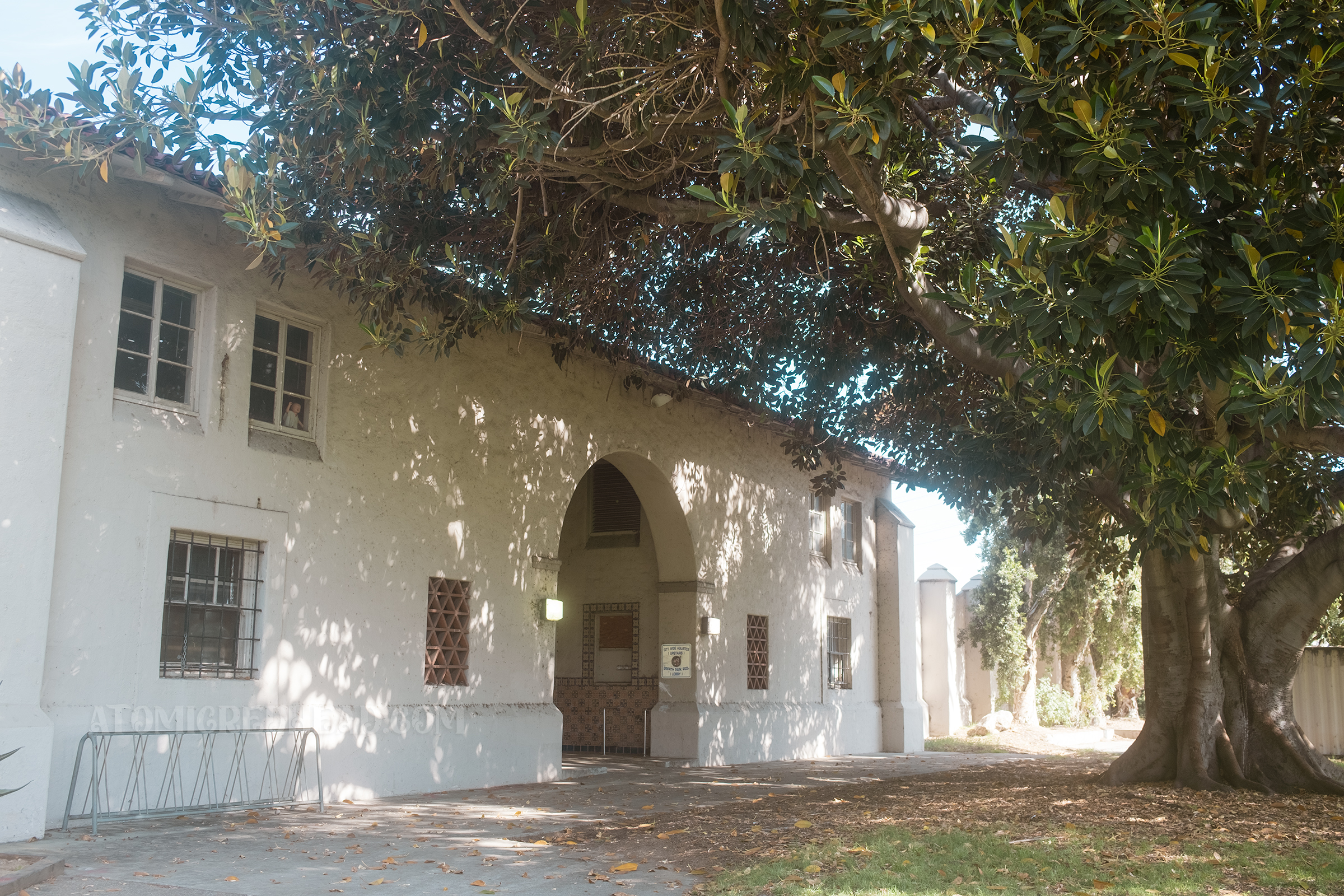 Angled view of the tan Spanish Revival style pool house with a large arched entry.