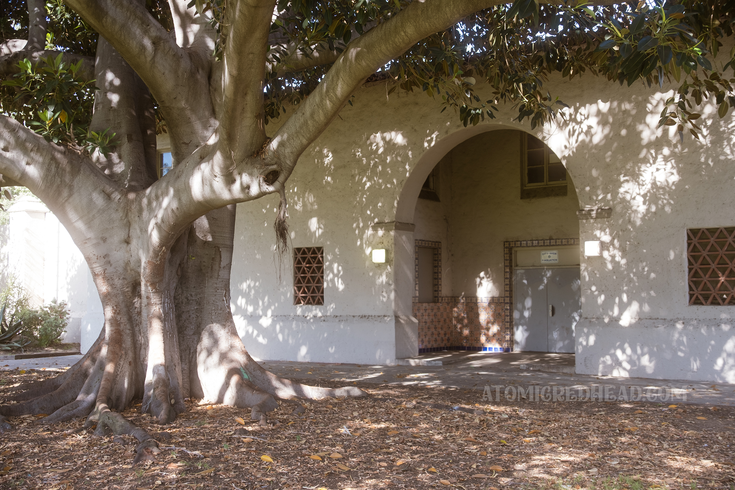 Angled view of the tan Spanish Revival style pool house with a large arched entry.