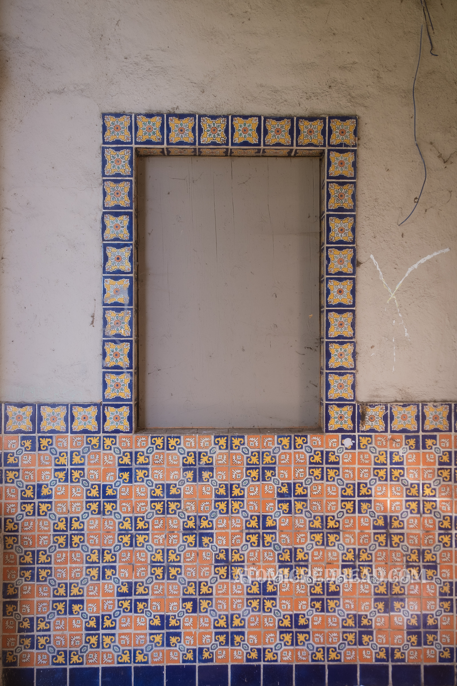 A small boarded up window features colorful tile around it.