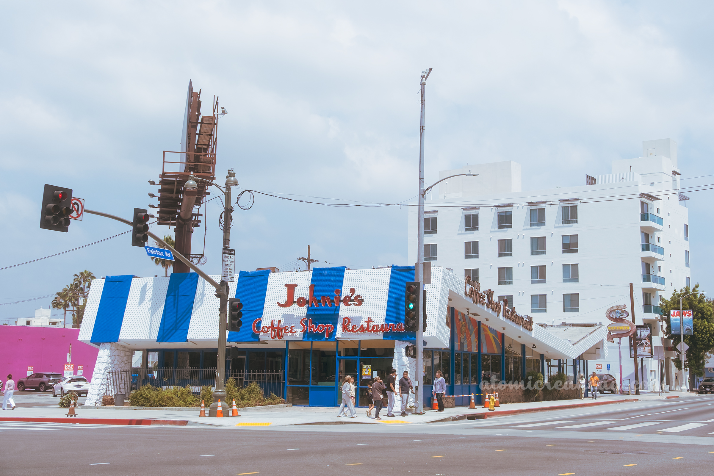 Angled view of the front of Johnie's Coffee Shop, a blue and stripe butterfly roof hangs low, with red letters reading "Johnie's Coffee Shop and Restaurant"