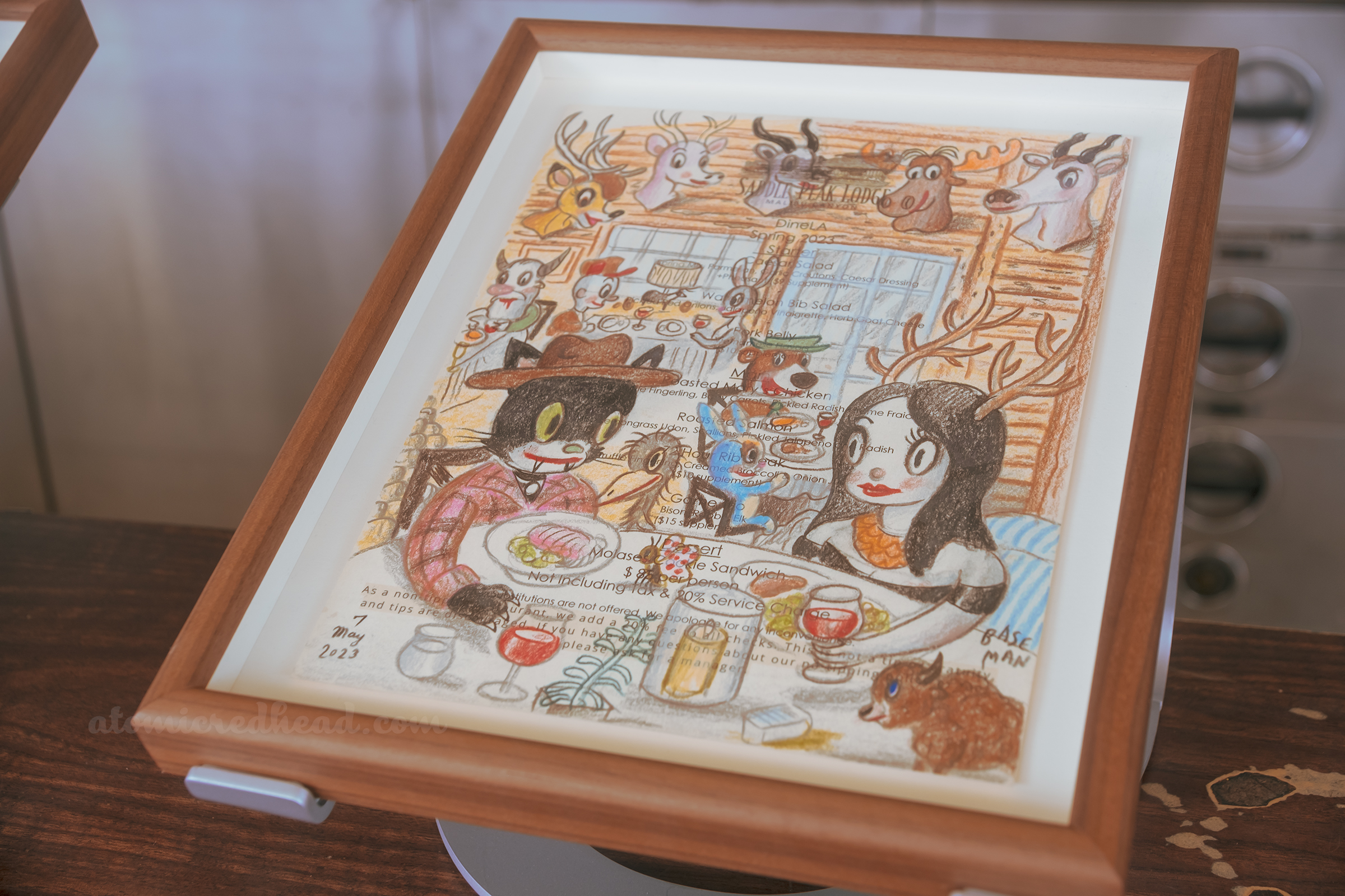 One of Baseman's works, this one features a dark haired woman dining with a black cat, in the background is Yogi Bear, and hanging on the wall are stuffed mounts of various animals.