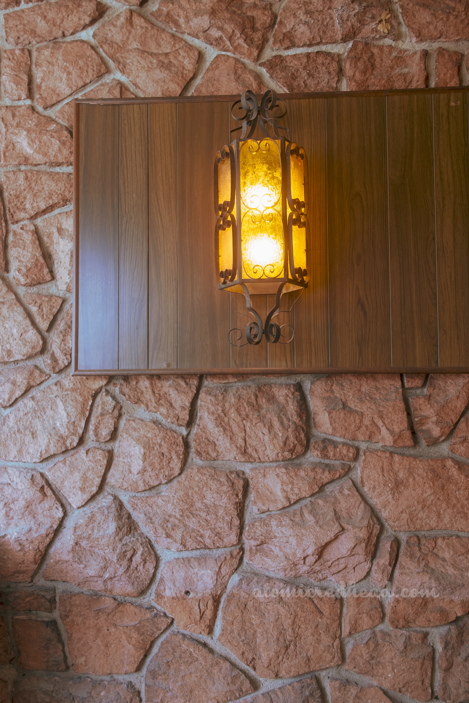 Close-up of a light fixture hanging on a wood panel against a rock wall.