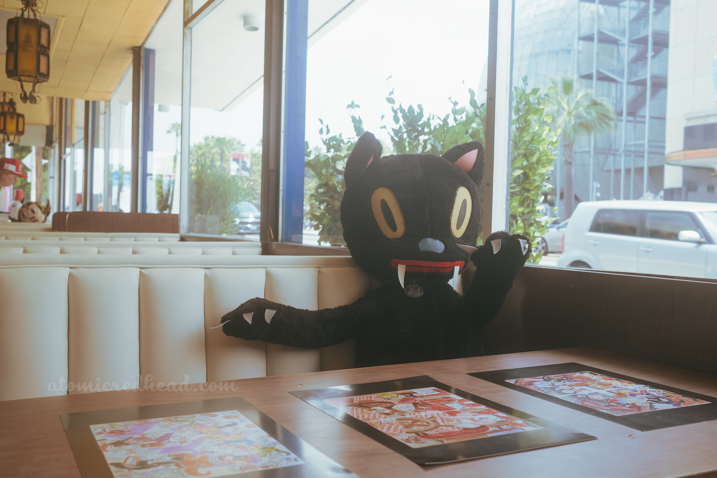 Close-up of a large stuffed black cat in Baseman's style, sitting at one of the booths.