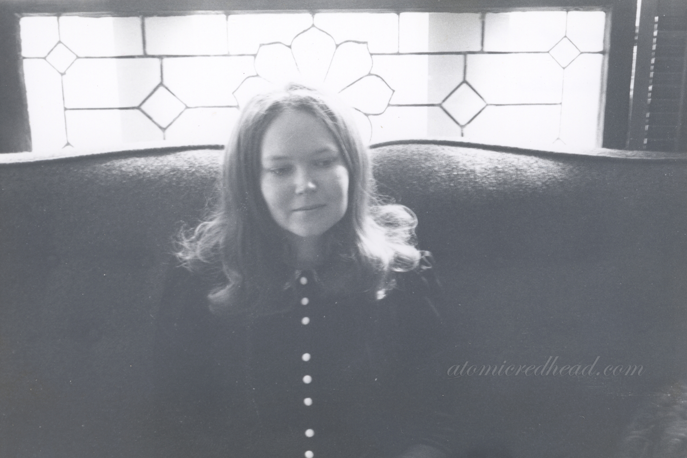 Black and white photo of my mom sitting on a couch in front of a leaded glass window.