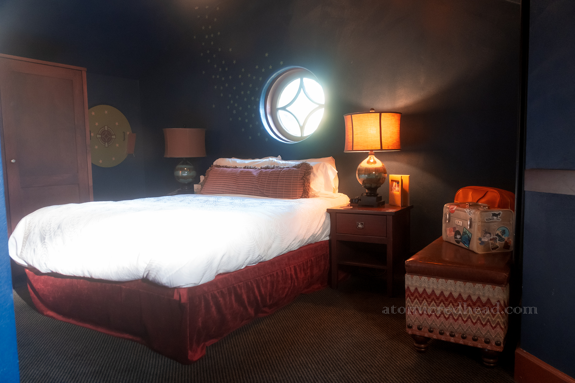 View of our room, painted in a dark, rich blue, with a round window above the bed, which is flanked by golden lights.