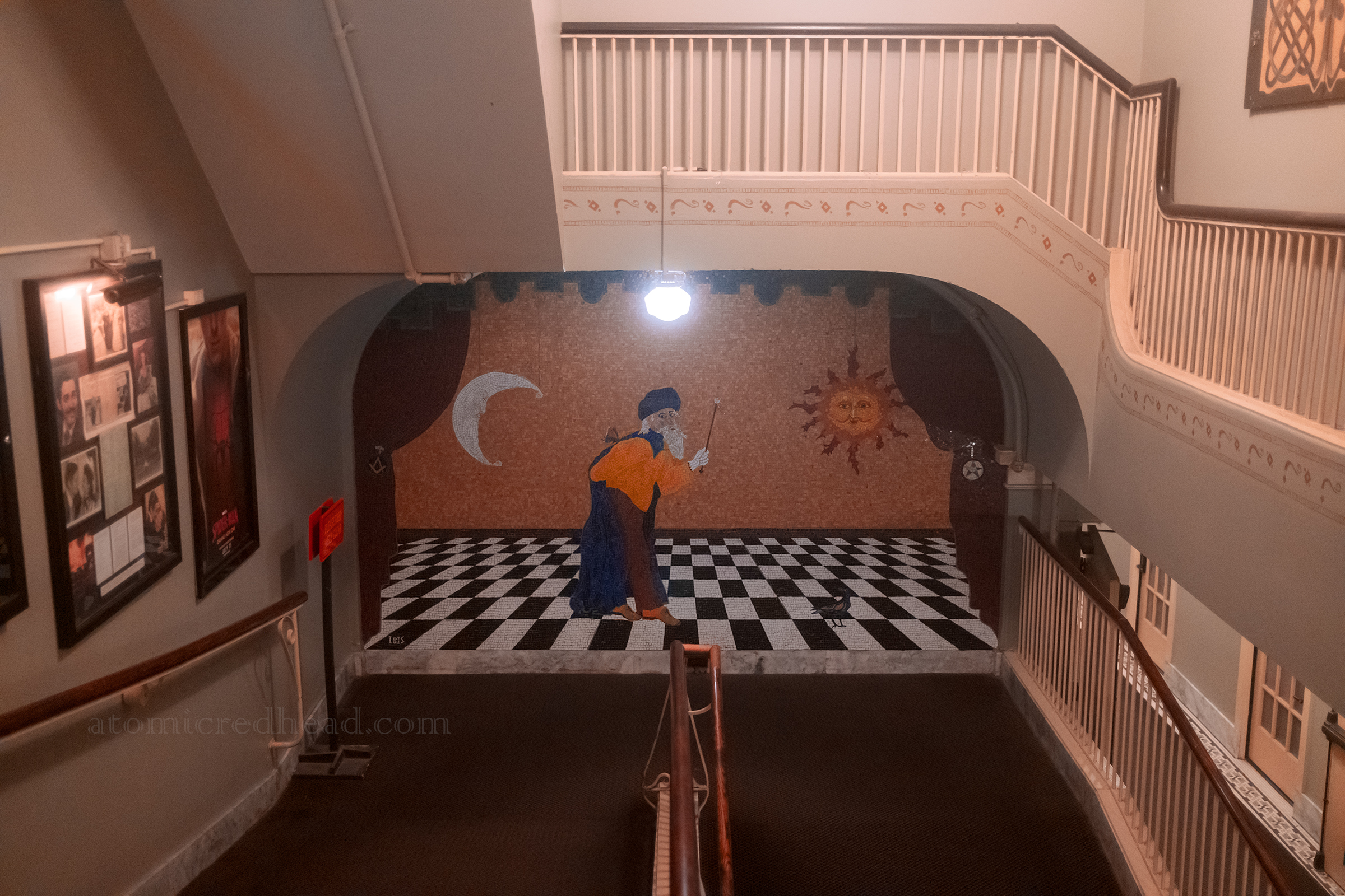 A large mural of an old man on a black and white checkered floor with a moon on the left and son on the right.