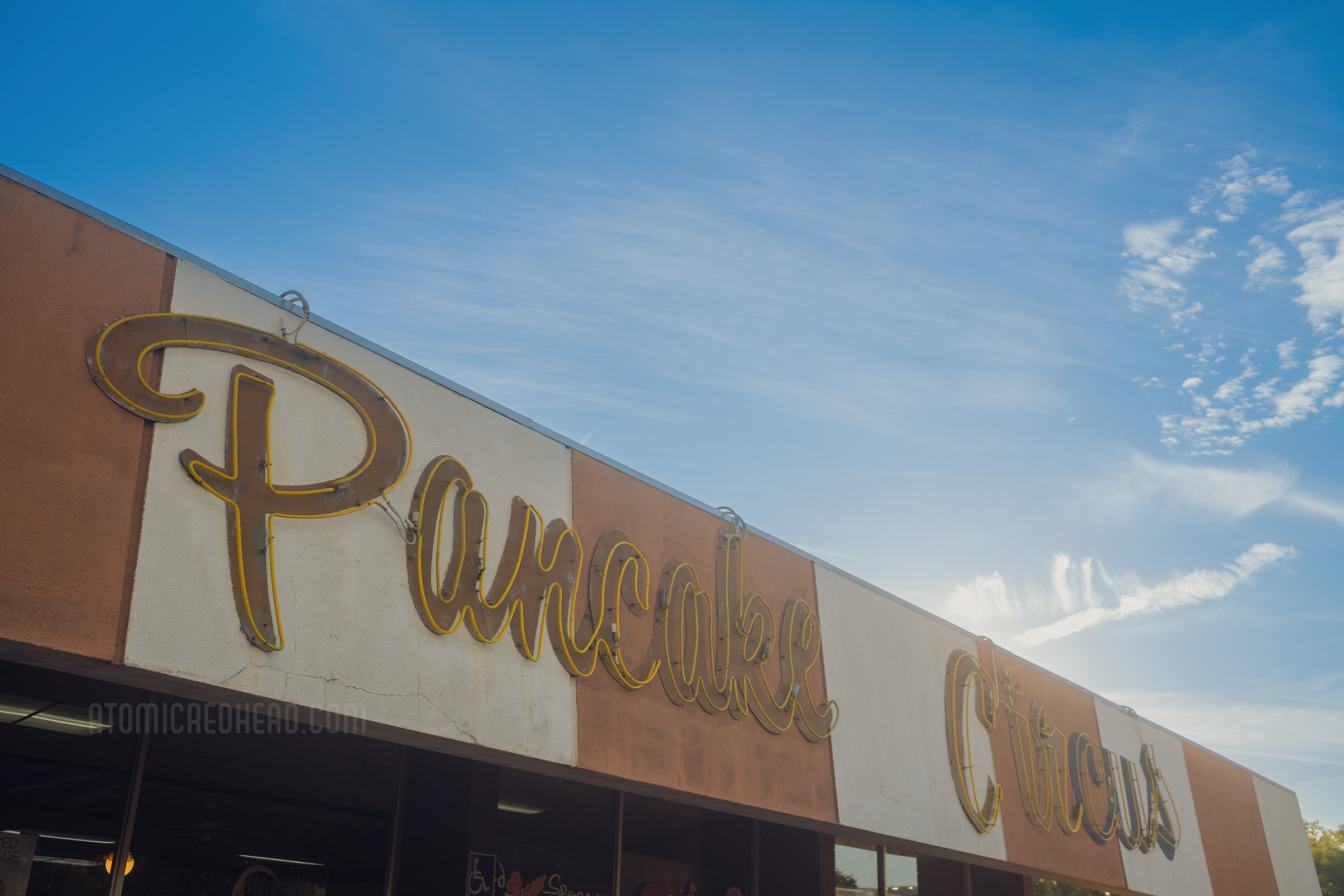 Close-up of the front of Pancake Circus. Red and orange stripes painted across the top, with a neon script reading "Pancake Circus" over the top.