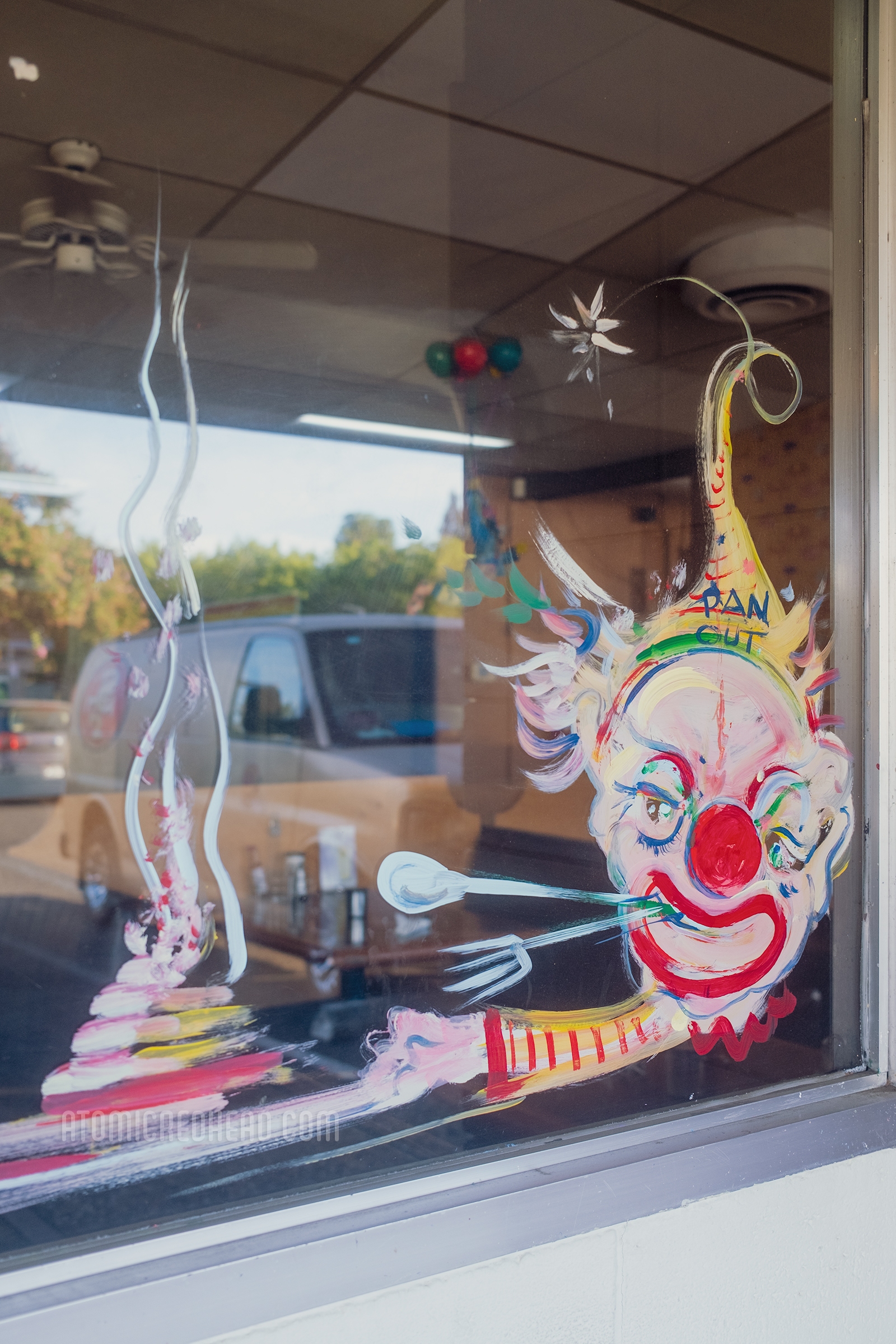 Close-up of one of the painted windows, a clown holds a spoon and fork in his teeth and in one hand he holds a plate with a stack of pancakes.