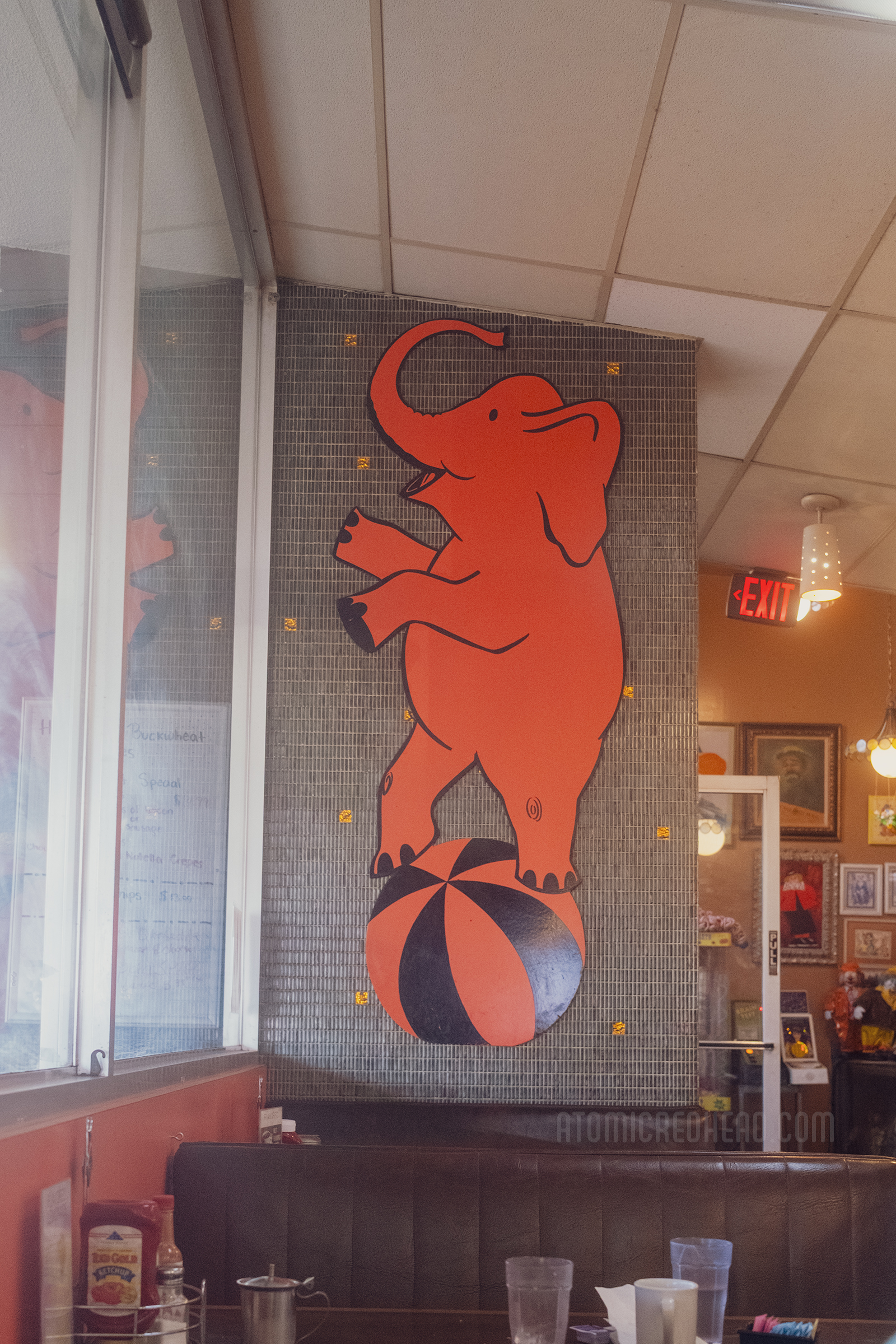 An orange elephant stands on a striped ball, painted on the wall.