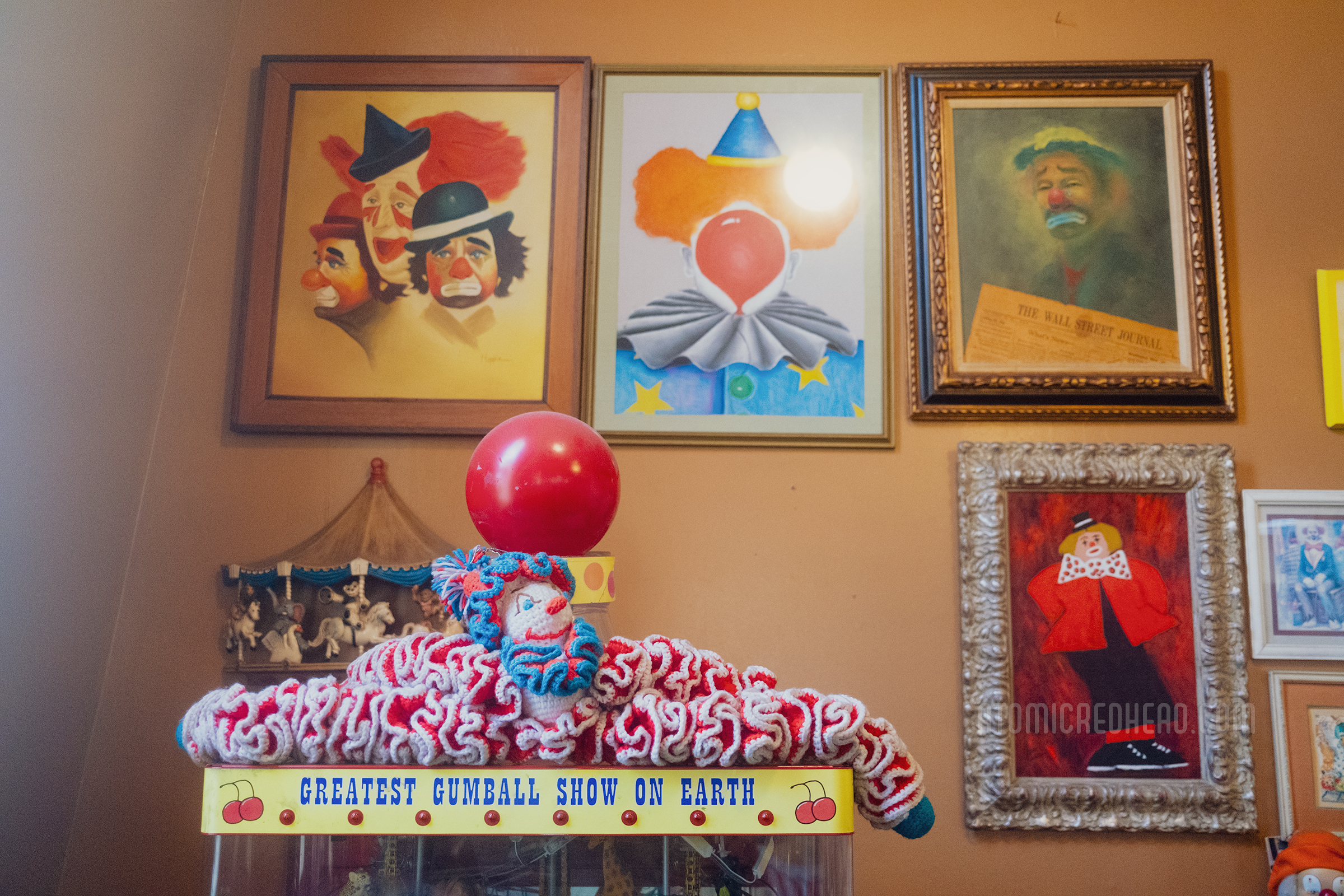 Various clown paintings hang on a tan wall just inside the door.