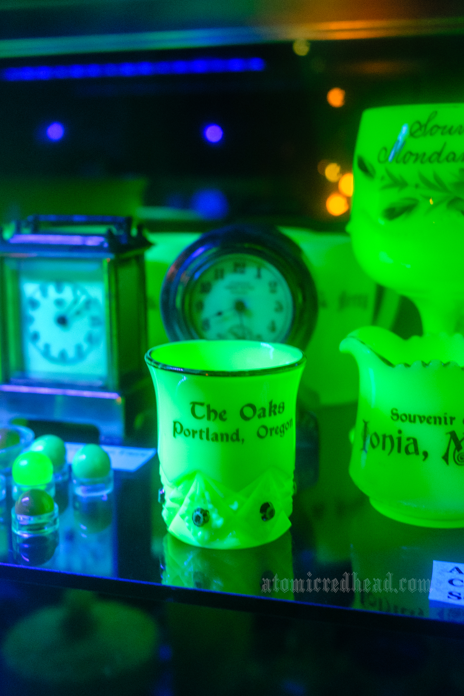 Pieces of uranium glass which glow green under blacklight. In the center is a small cup that reads "The Oaks Portland, Oregon" 