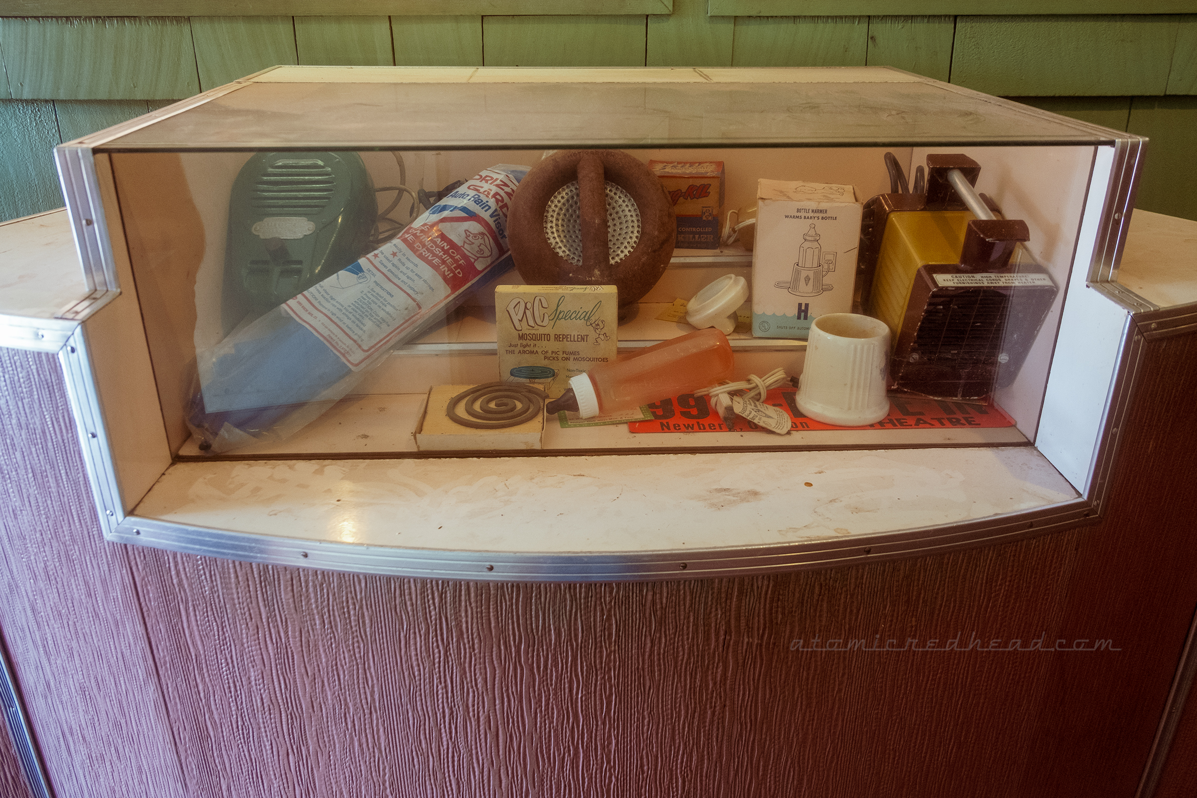 A display case shows vintage drive-in items, such as a rain guard for the windshield, a vintage speaker, a portable heater, and event a bottle warmer for the car.