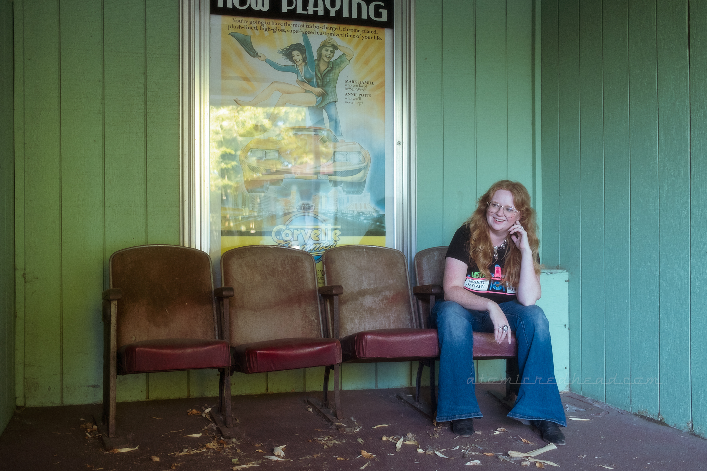 Myself seated in some old theatre seats outside the concession stand, behind me a poster advertises the movie Corvette Summer.