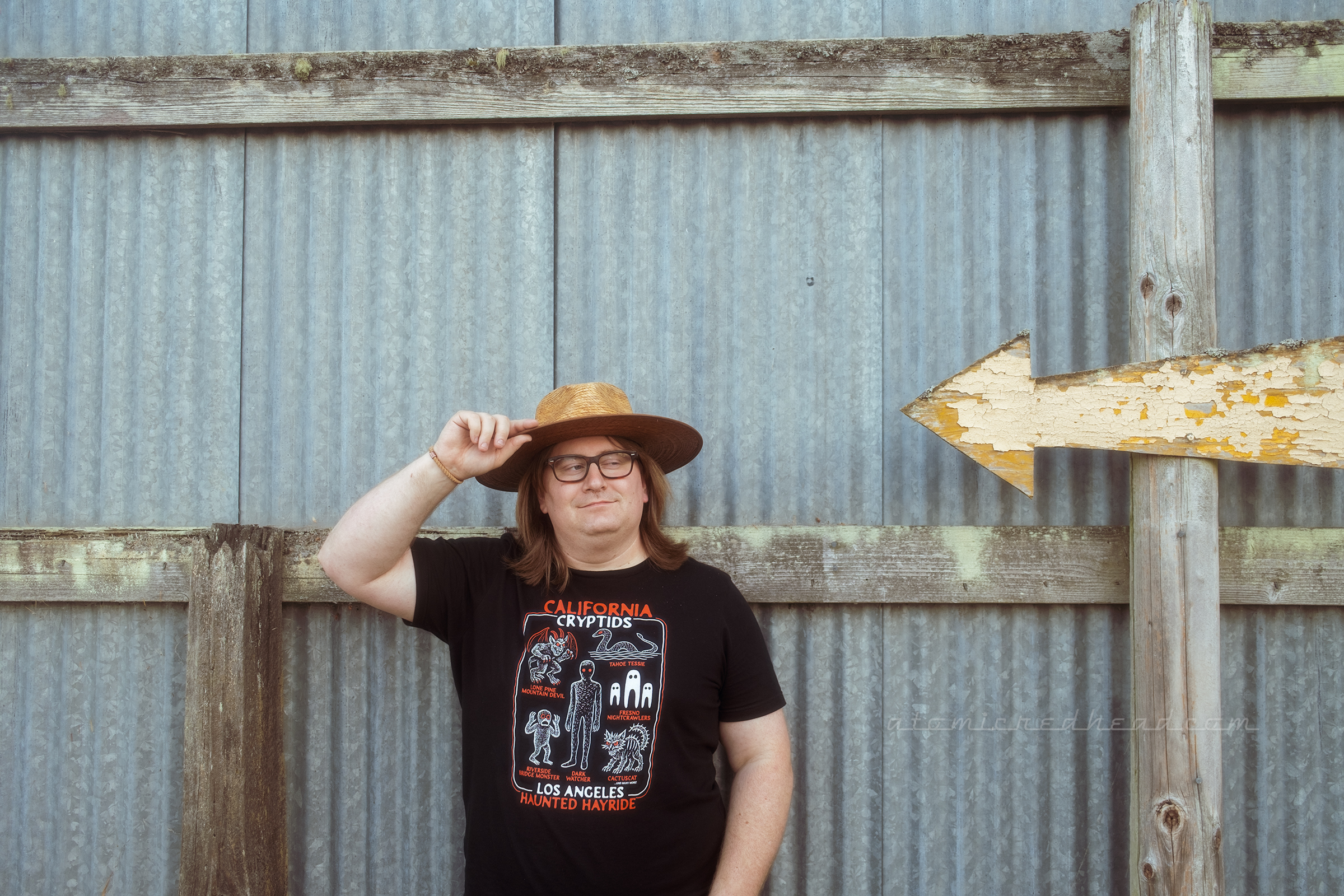 Patrick leans against a corrugated metal wall with a yellow arrow pointed at him.
