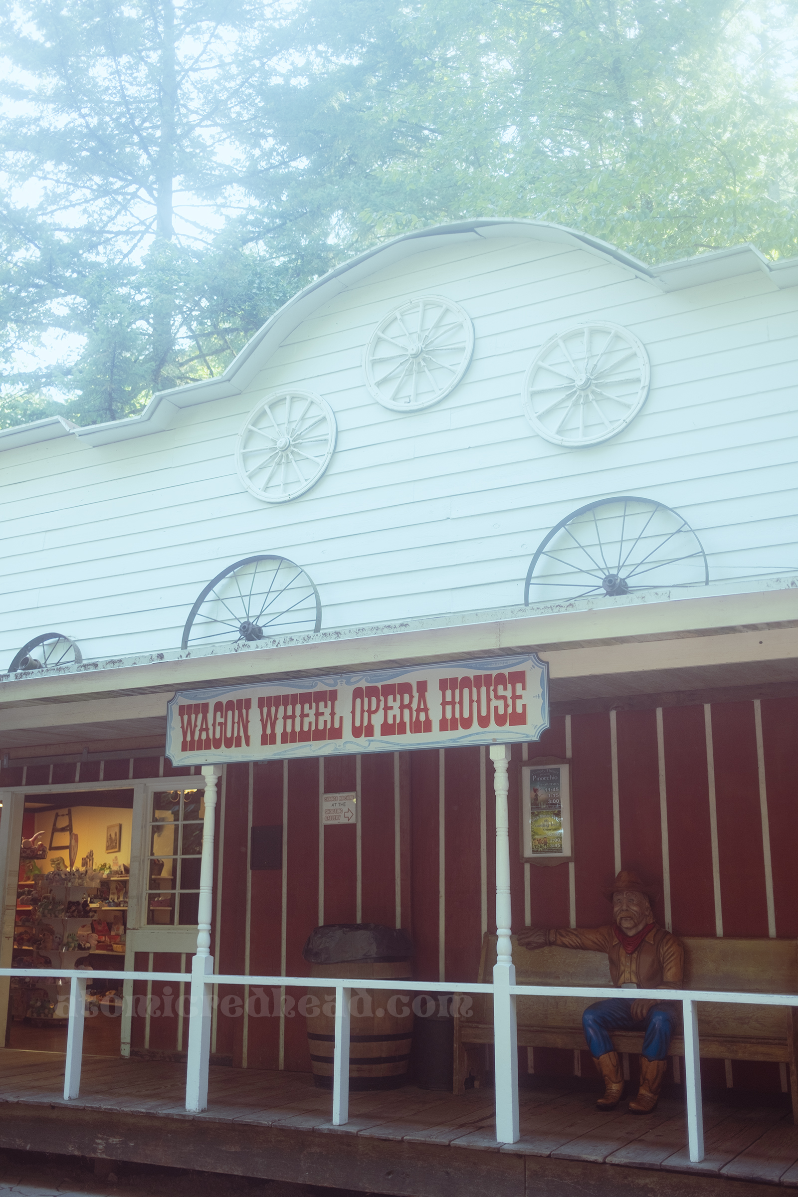 A large white and read building has wagon wheels hanging on it and a sign reading "Wagon Wheel Opera House"