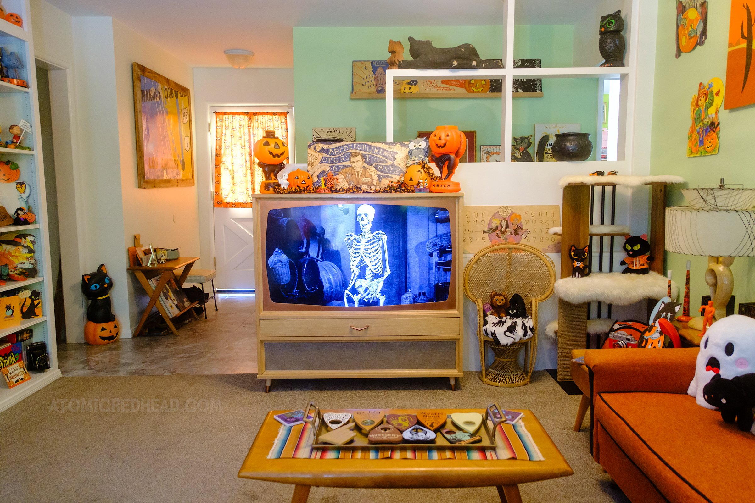 View of our TV with House on Haunted Hill on the screen. On top sits a spirit board with a Twilight Zone theme, featuring Rod Serling and icons from the show, it is surrounded by vintage plastic jack o'lanterns.