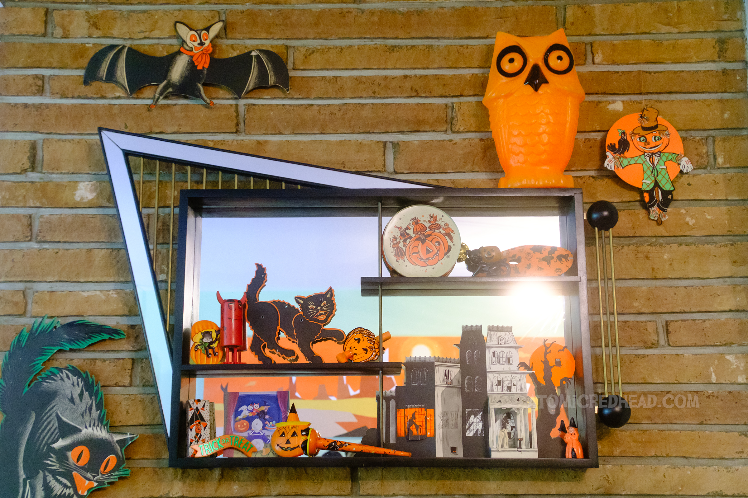 An asymmetrical mirrored shadow box hangs above our fireplace. Atop sits a vintage blow mold owl, inside sits a small paper haunted house, a black cat, and some vintage noise makers with a Halloween motif.